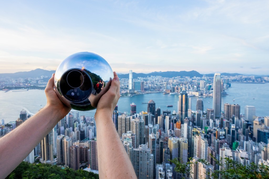Person holding Worldcoin Orb over Hong Kong skyline.