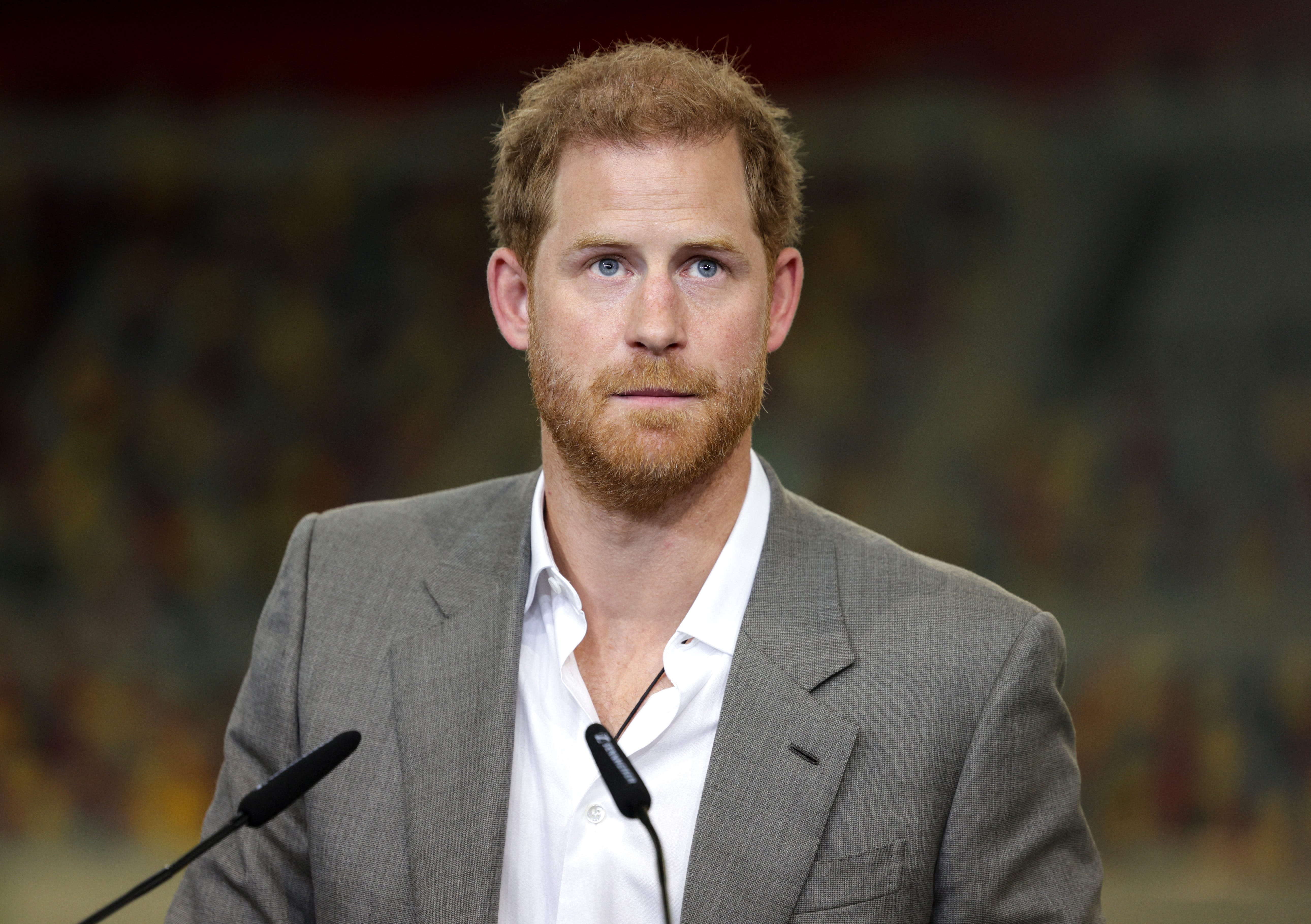 Prince Harry speaks into a microphone in a gray jacket and a white shirt