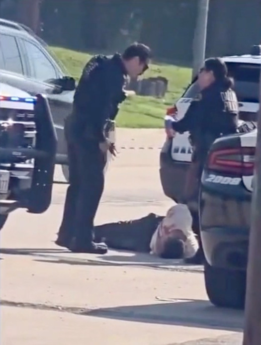 Police officers attending to a man lying on the ground.