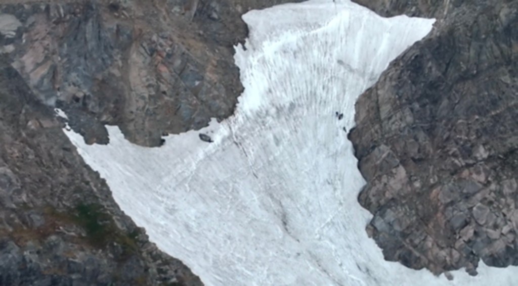 Aerial view of a snowfield nestled between dark rock faces.