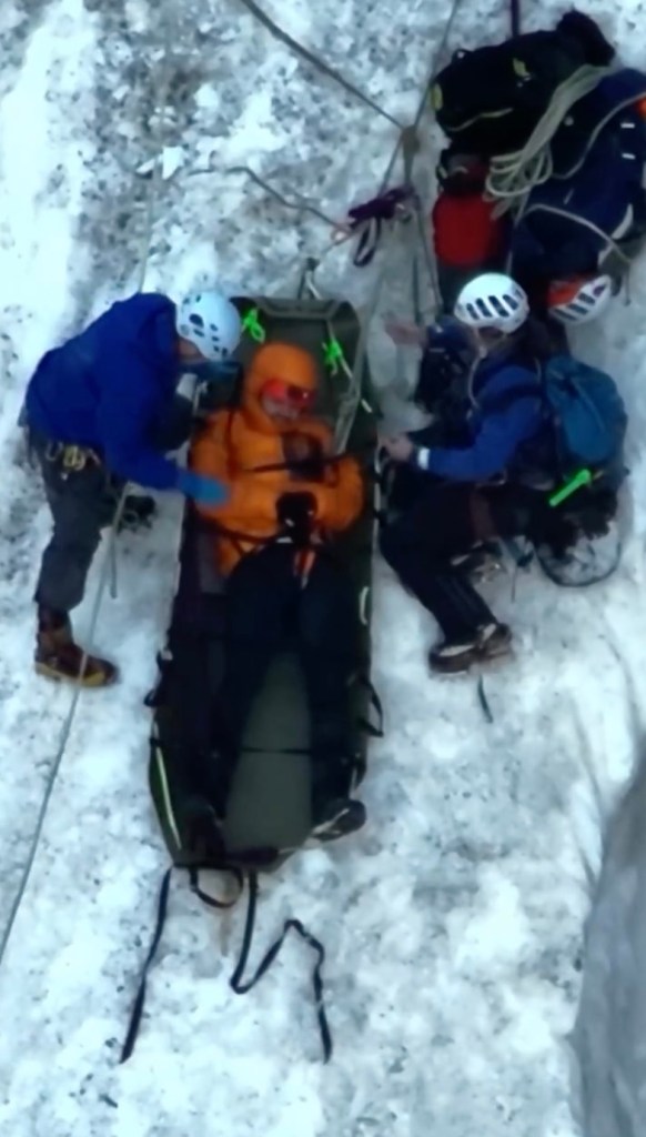 Rescue workers securing an injured climber on a snowy mountainside.