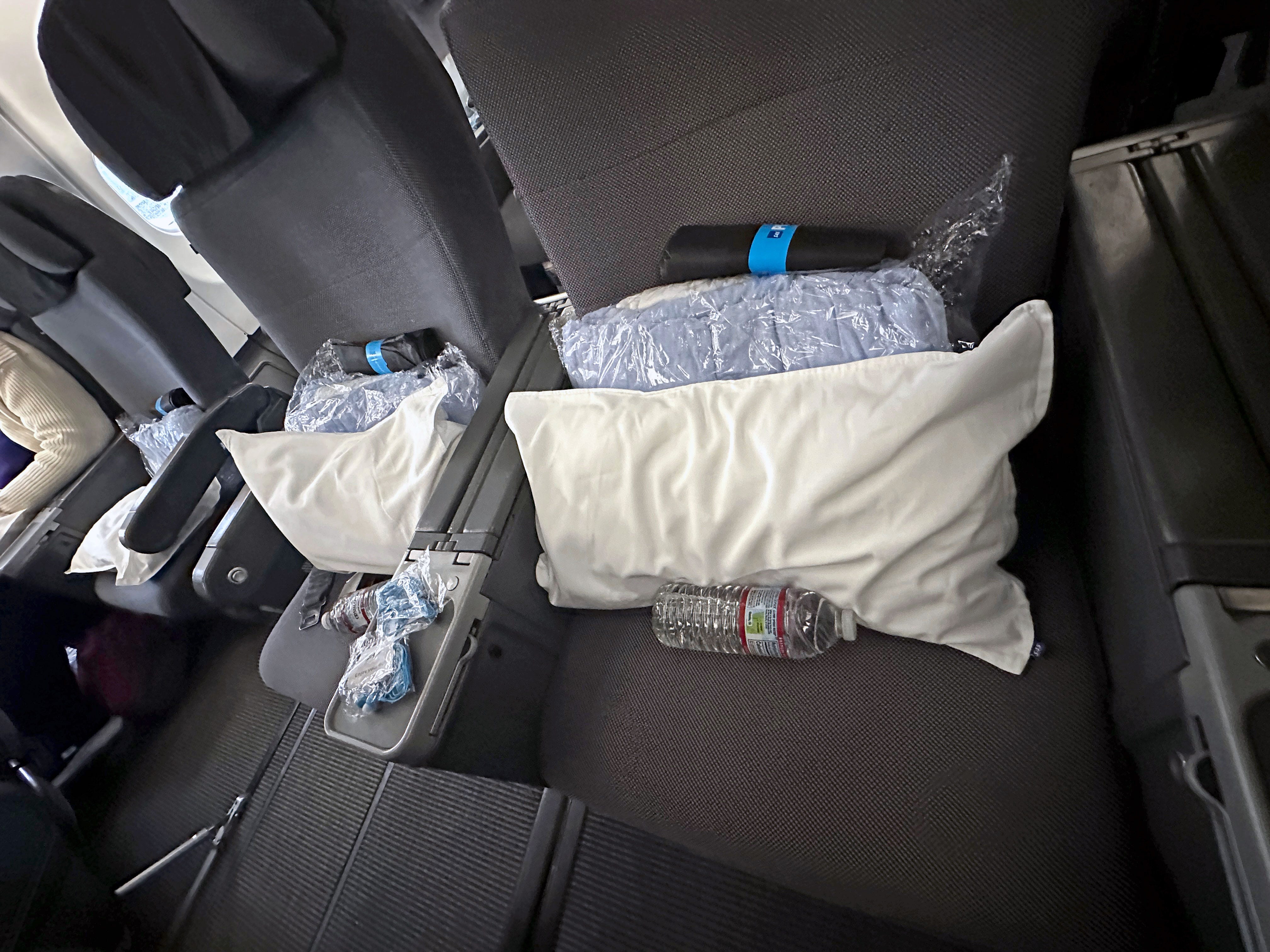 Two airplane seats with pillows, blankets, an amenity kit, and water bottles.
