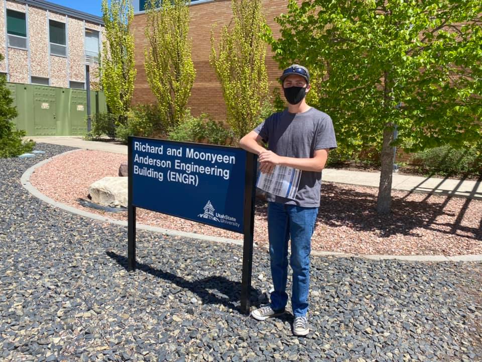 Person wearing a mask standing by a sign for the Richard and Moonveen Anderson Engineering Building.