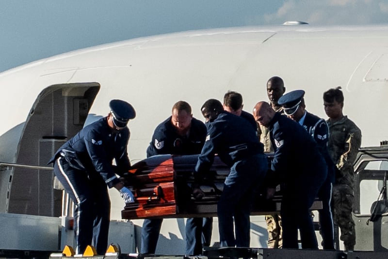 Men in Air Force uniform carry a coffin out of a white plane.