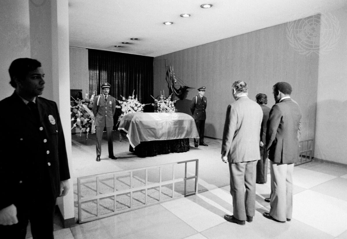 People pay their respects before a flag-draped coffin guarded by security.