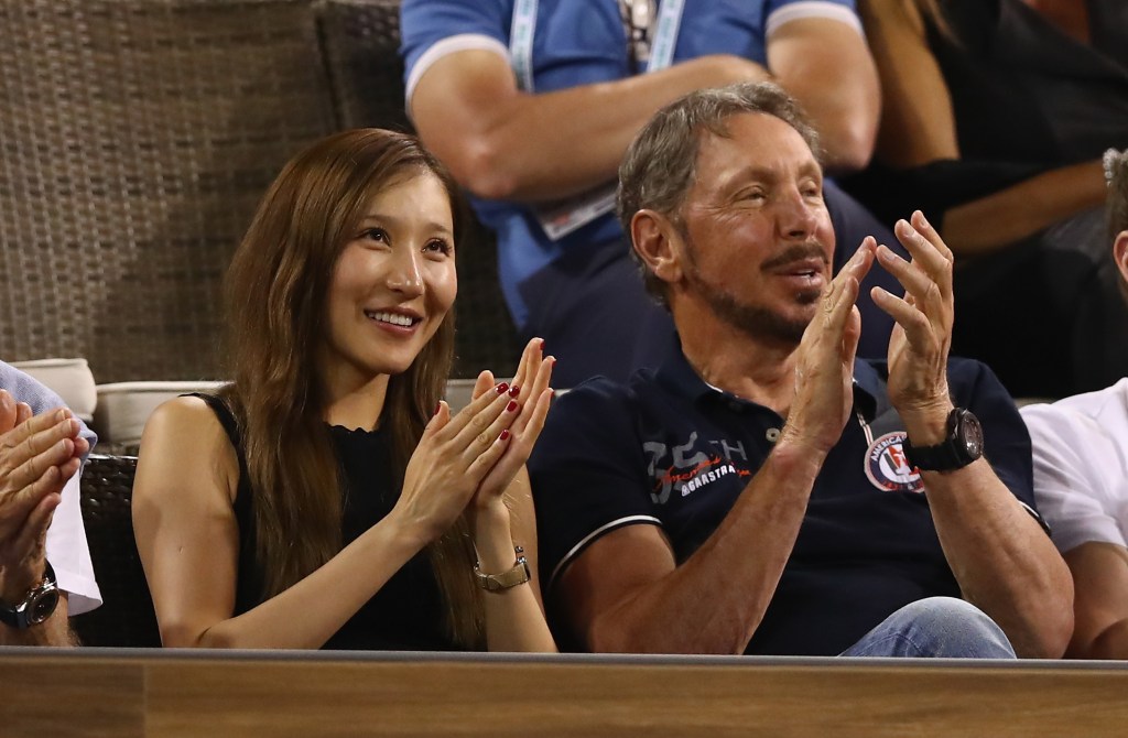 Larry Ellison and a woman applaud at a tennis match.