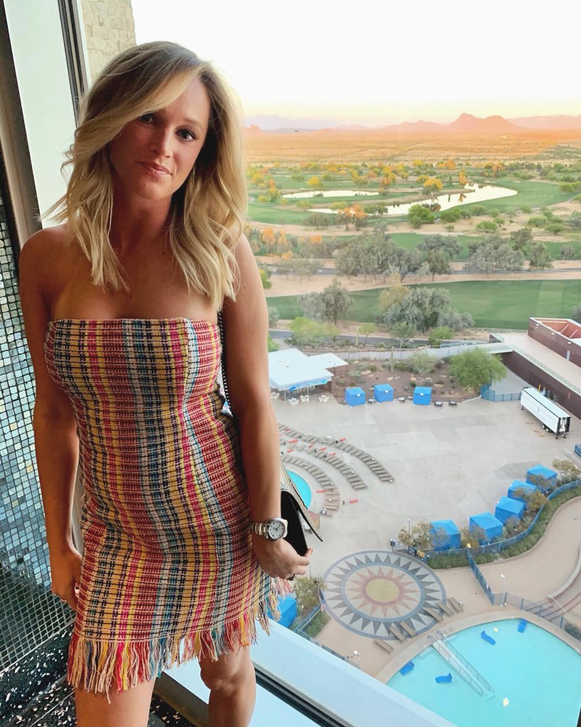 Woman in colorful dress standing by window overlooking golf course and resort pool.