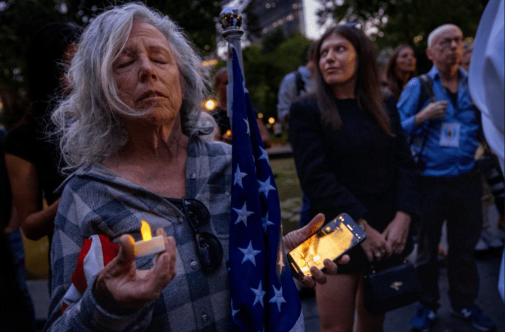 Woman holding a candle and a phone at a vigil.