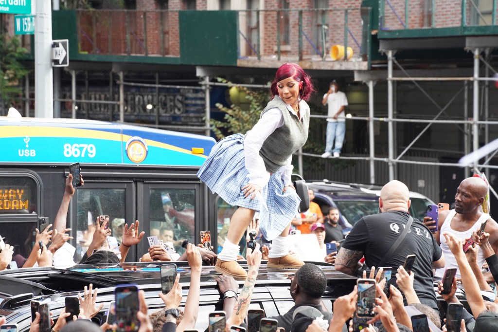 Cardi B standing on a car, surrounded by a cheering crowd taking photos.