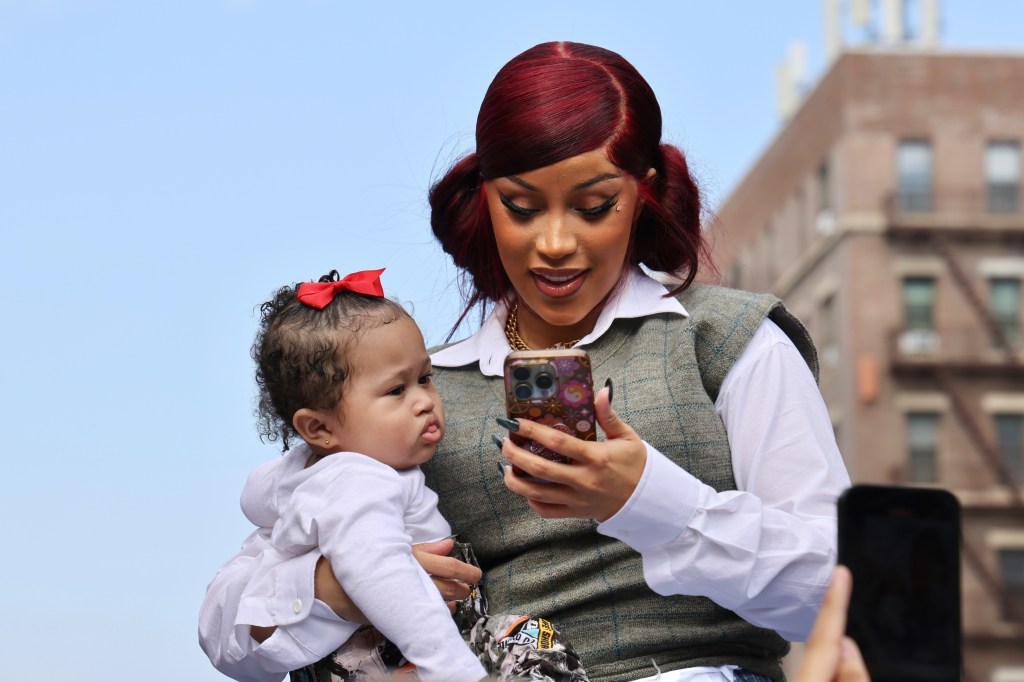 Cardi B holding her baby and looking at a phone.