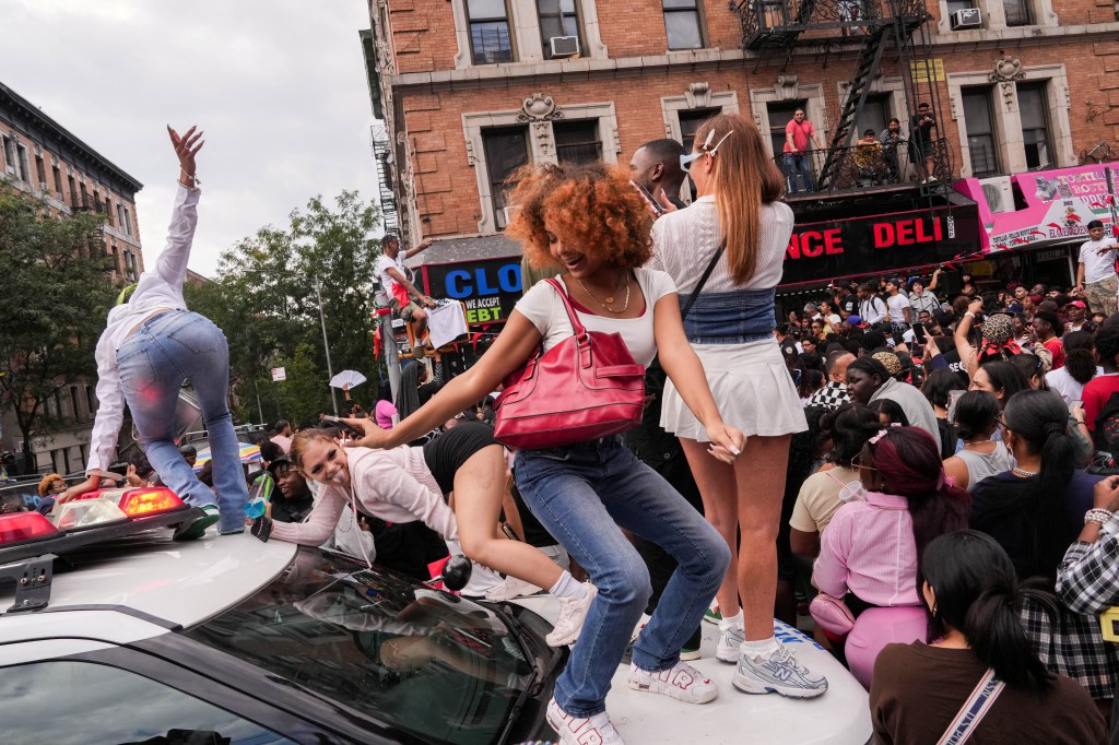 People dancing on a police car at a Cardi B pop-up event.