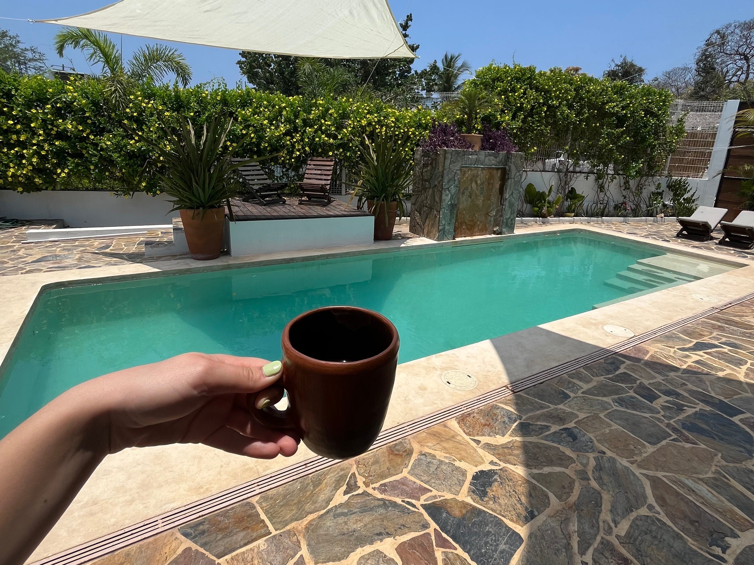 Hand holding coffee cup over blue-green pool