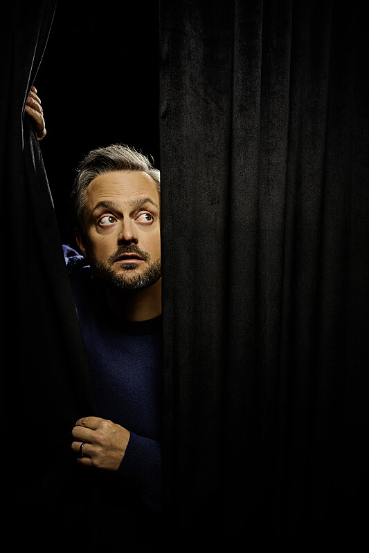 Nate Bargatze peering behind a curtain