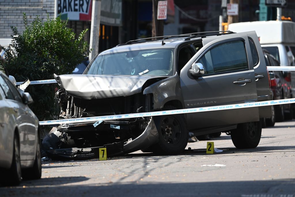 A damaged SUV at a crash scene, marked with police tape and evidence markers.