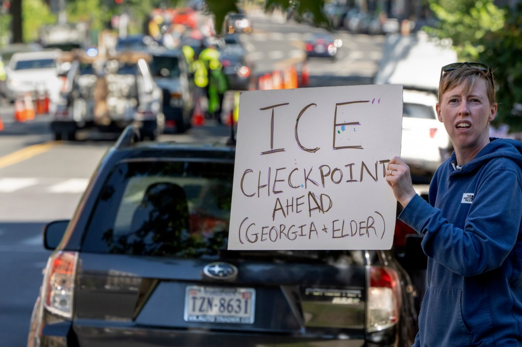 Protestor holds sign warning of ICE checkpoint ahead on Georgia Avenue and Elder Street.