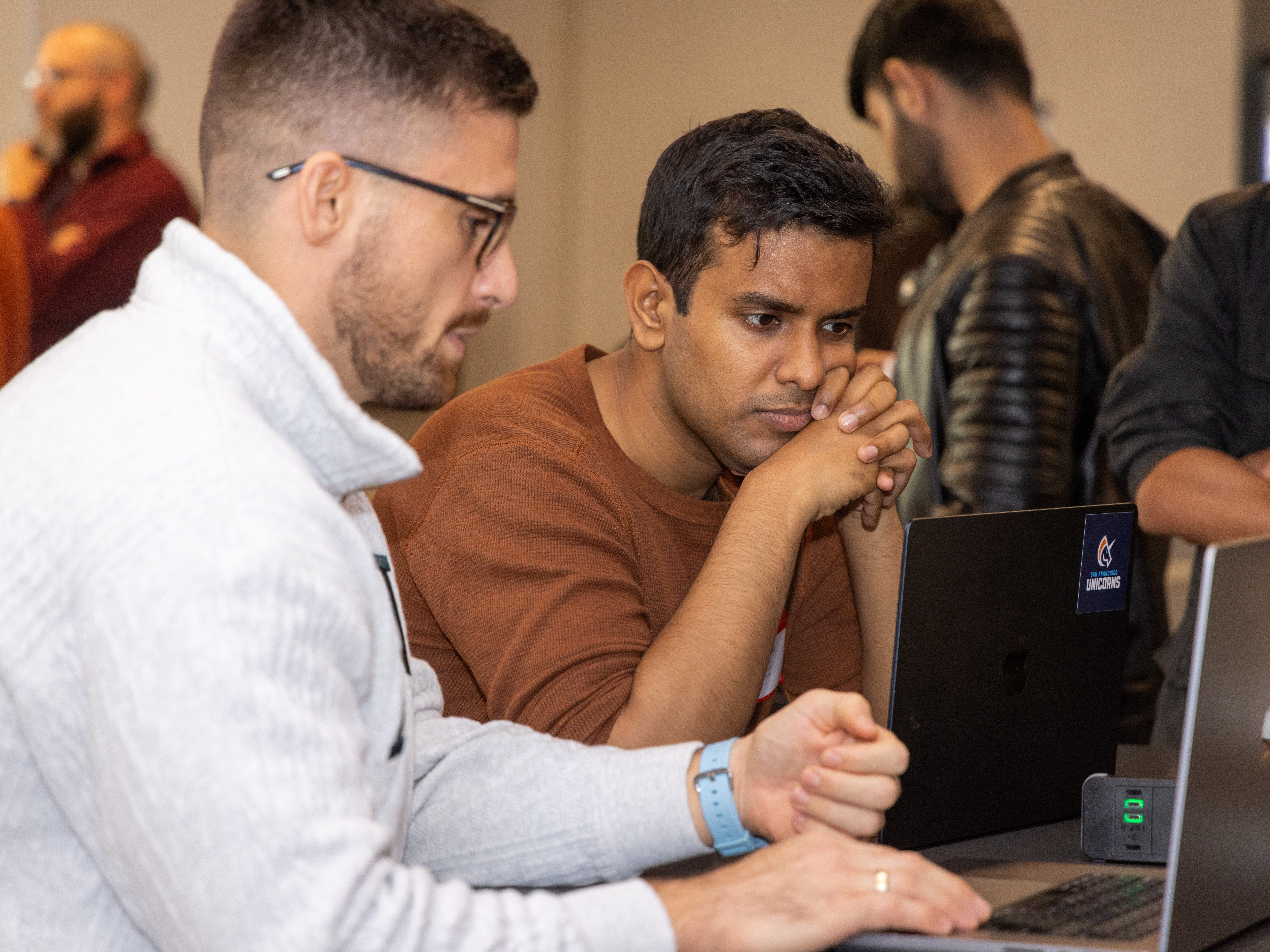 Two men look at a laptop computer screen.