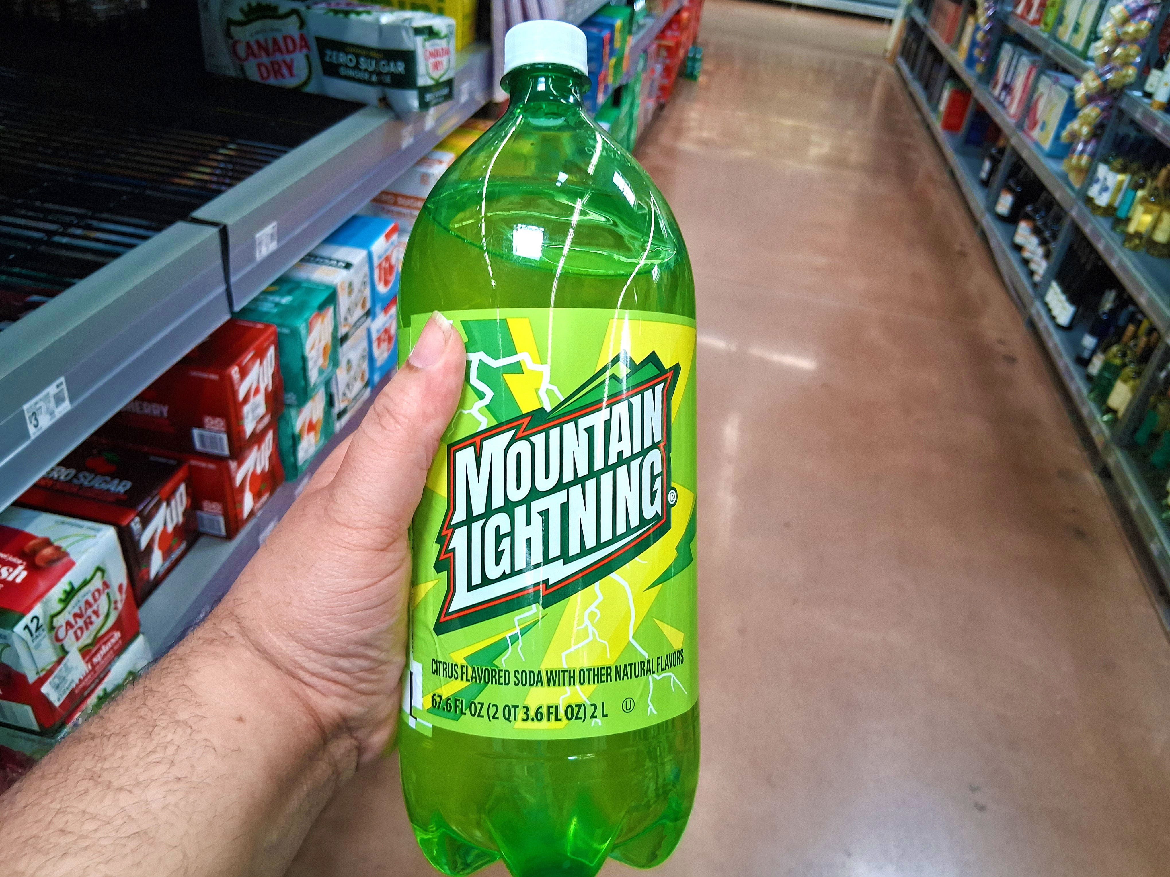A hand holding a bottle of Mountain Lightning soda.