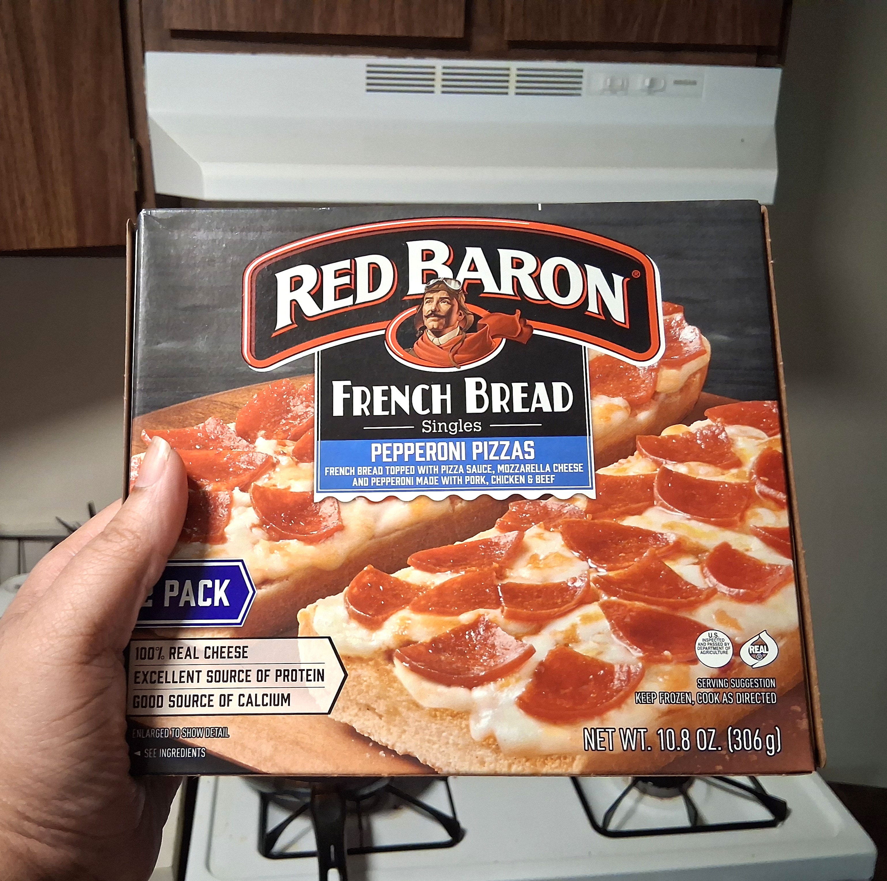 A hand holding a box of Red Baron pepperoni French bread pizza.