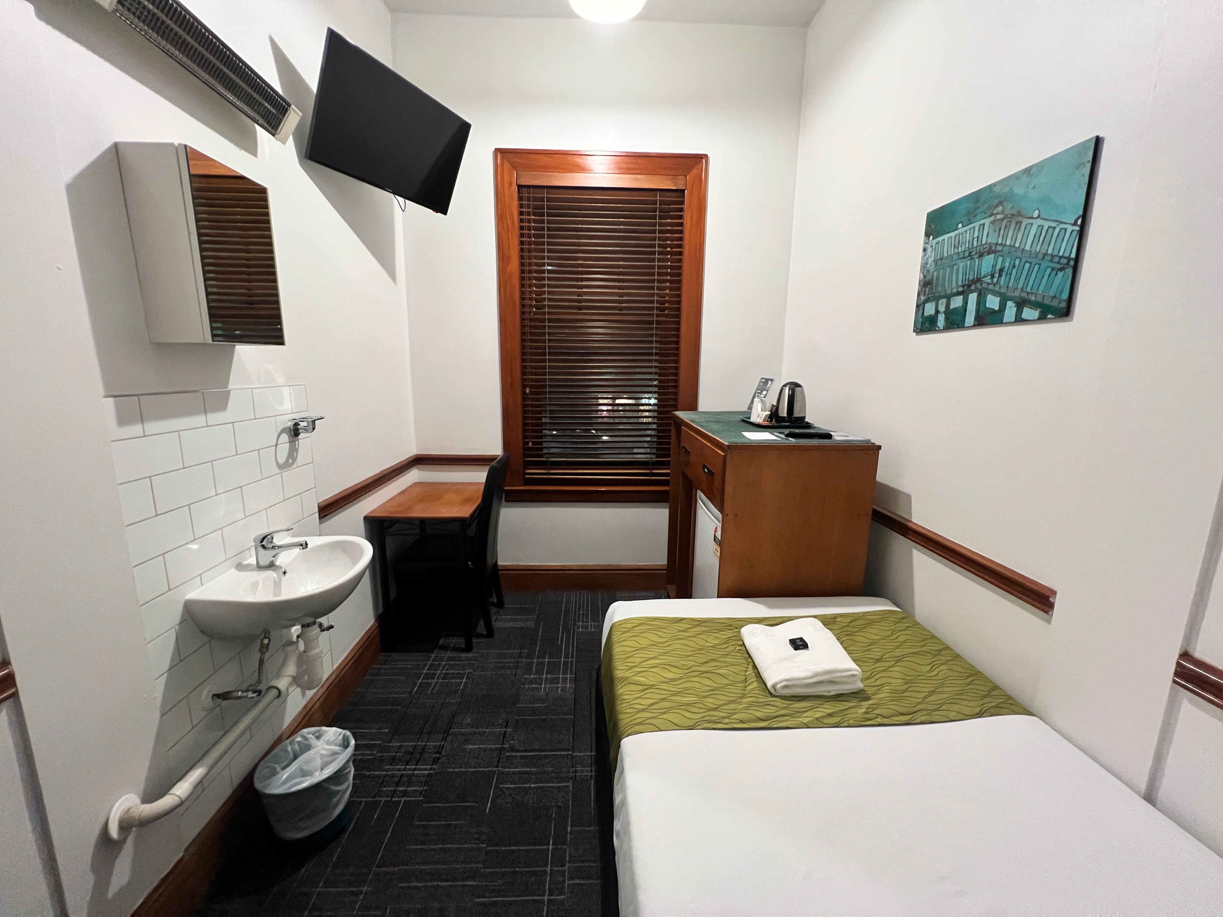 A private hotel room with a bed, sink, and dresser.
