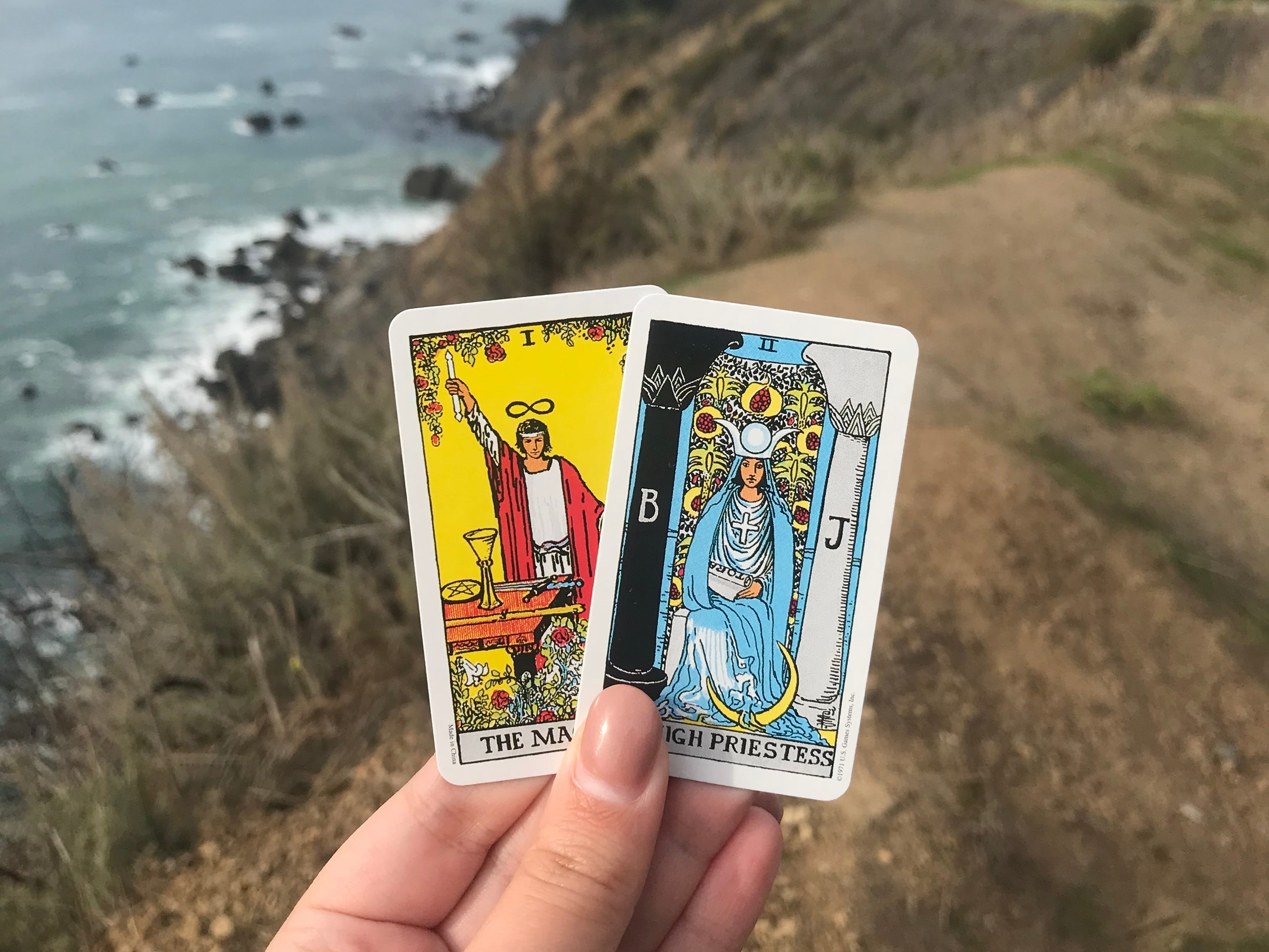 The author holding two tarot cards with the ocean in the background.