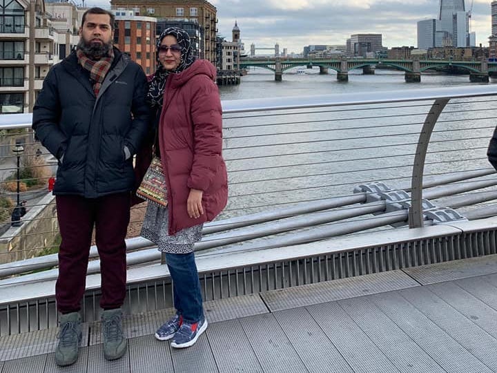 A couple stands on a bridge overlooking a city.