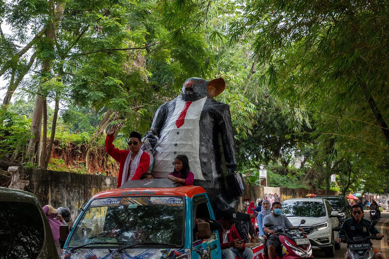A large rat float appears below trees on top of a red truck.
