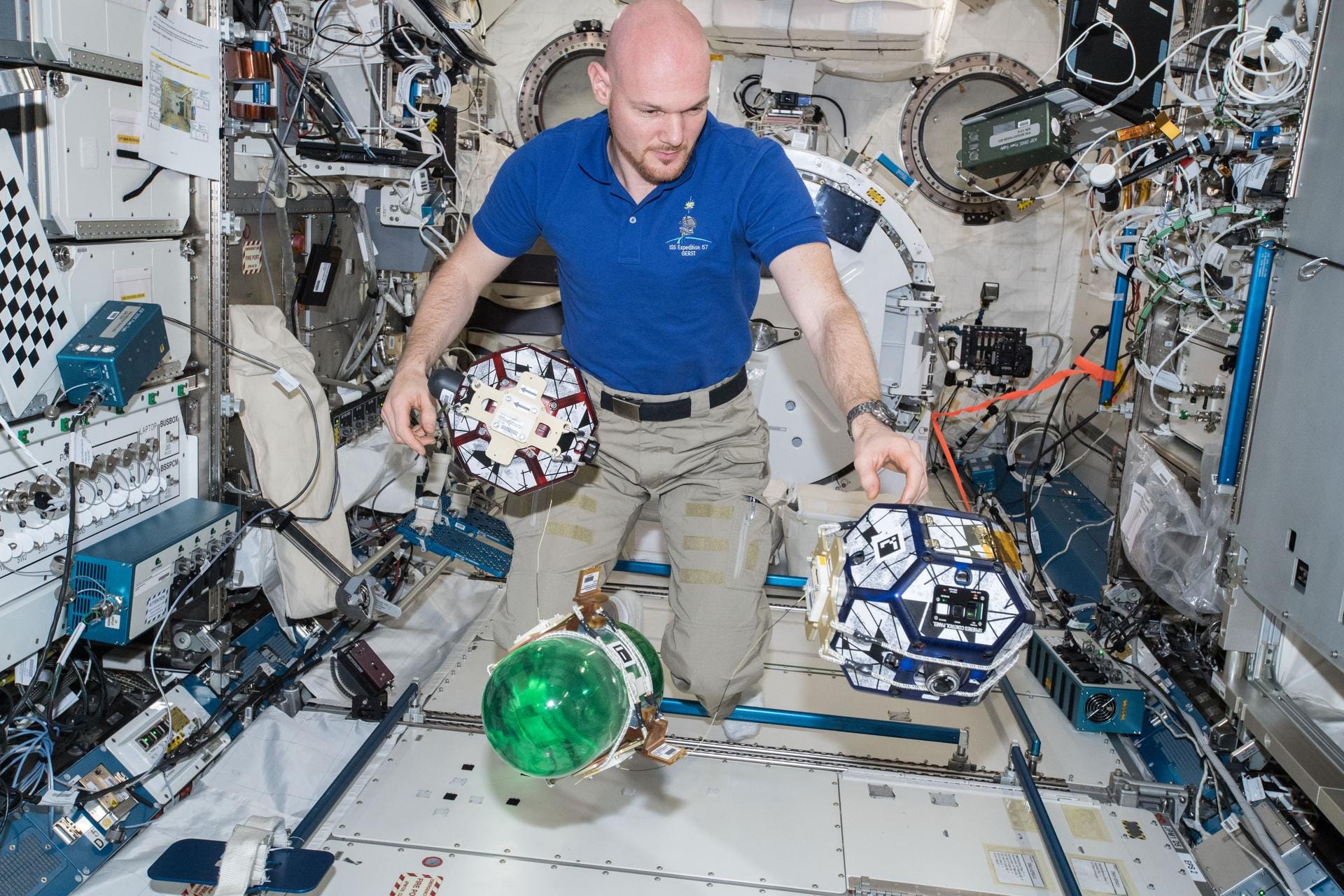 An astronaut floats surrounded by several oddly shaped devices, one with a green bubble on it