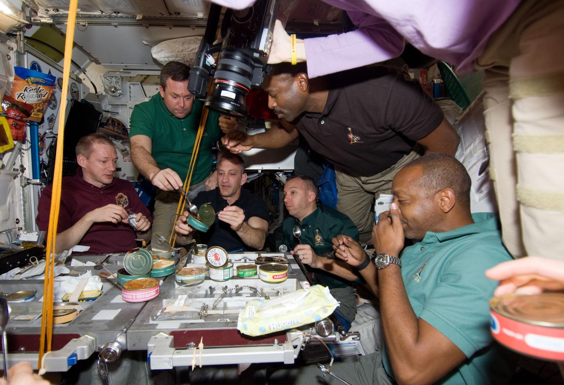 People gather around a table with tins of food on it on the ISS