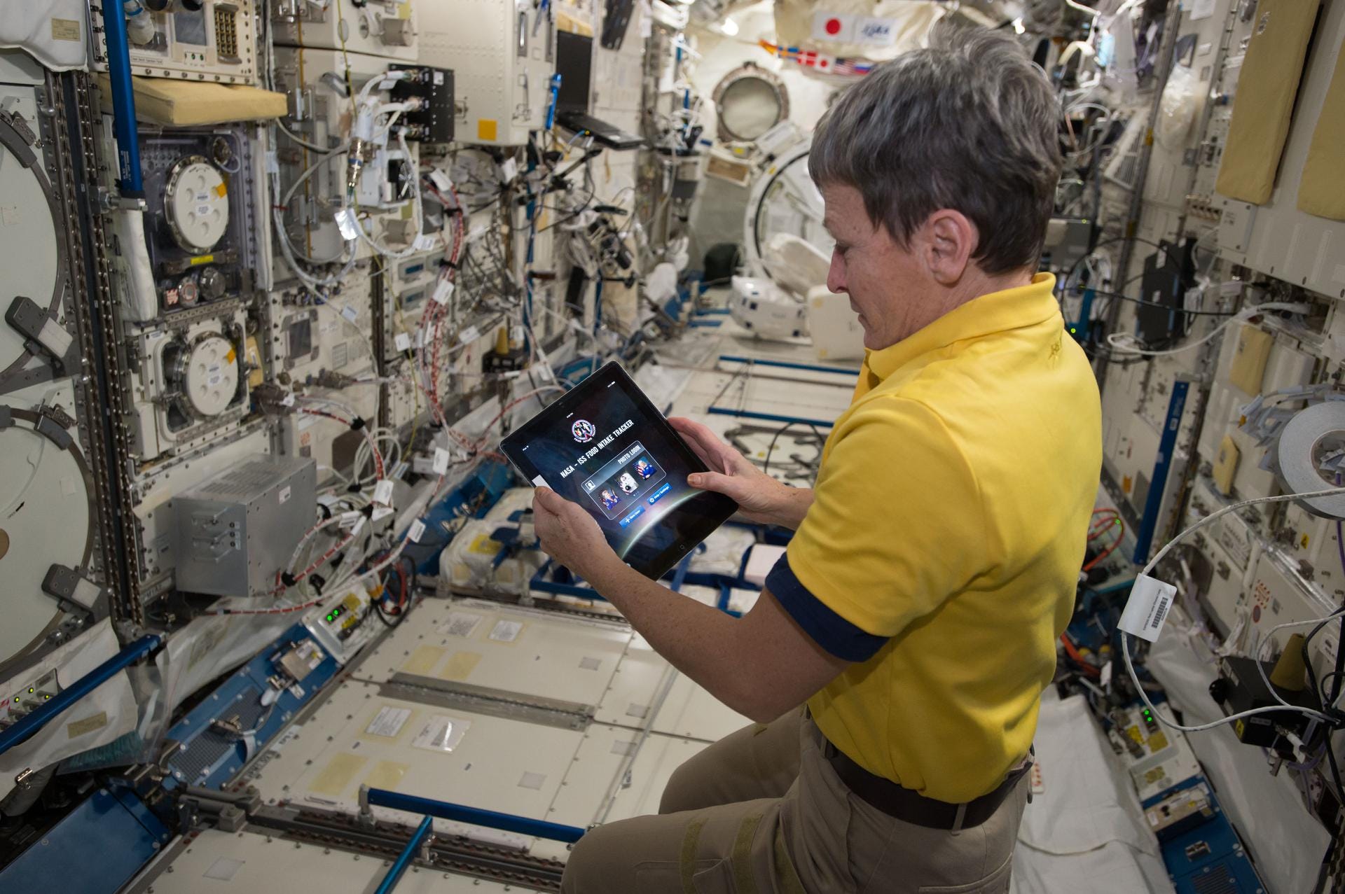 A woman in a yellow shirt looks at an iPad on the ISS