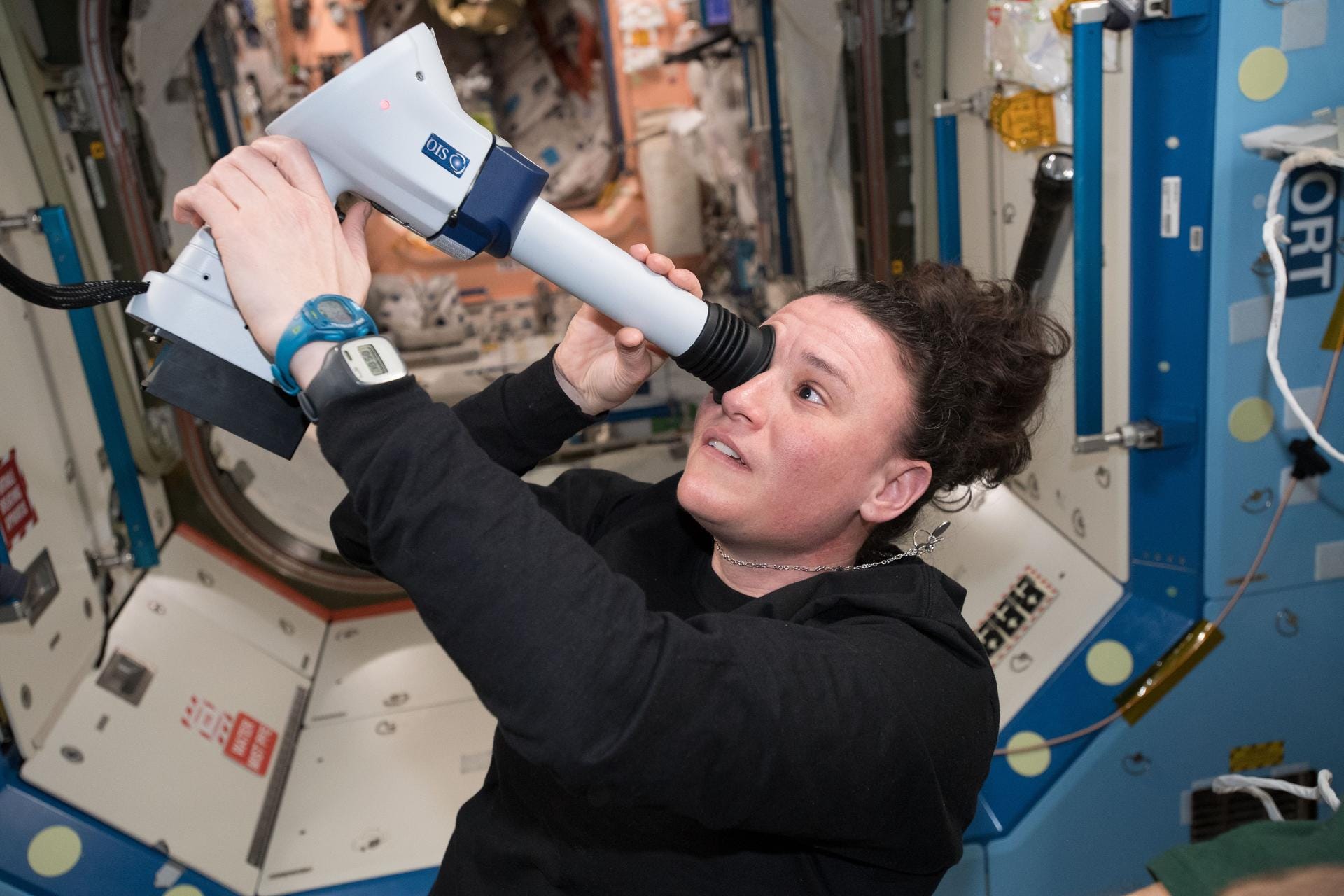A woman holds a medical device to her eye on the ISS