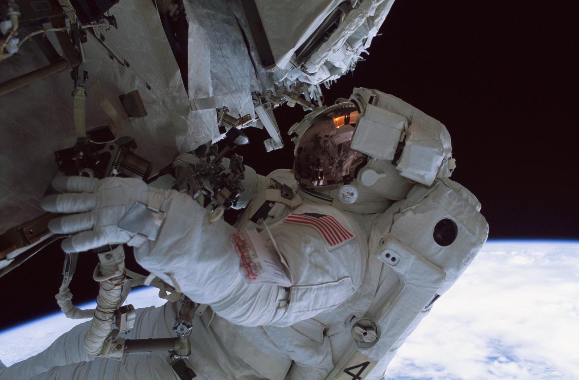 An astronaut in a spacesuit above the Earth, holding onto the ISS