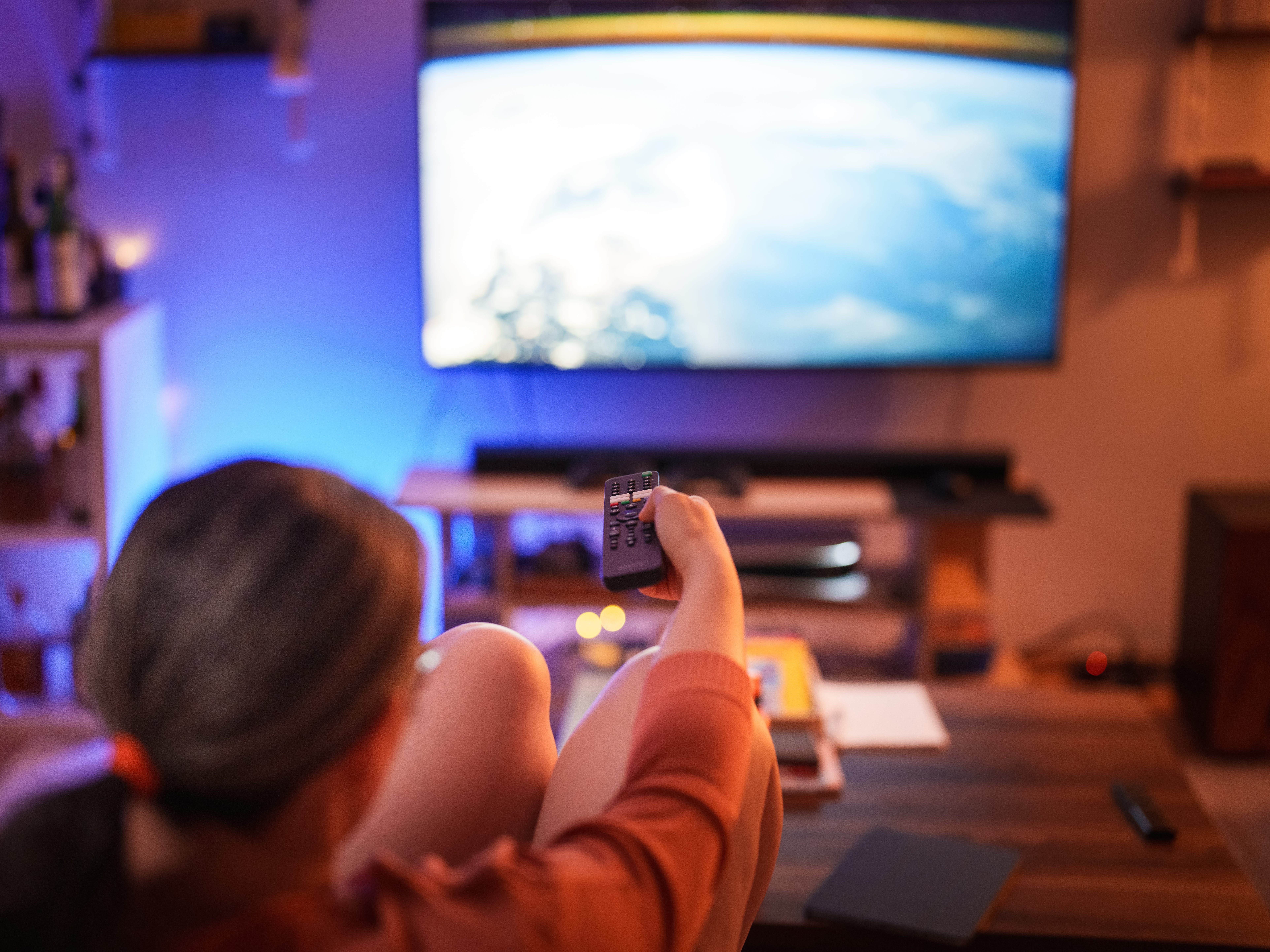 A woman sitting on a couch in front of a TV holding a remote.