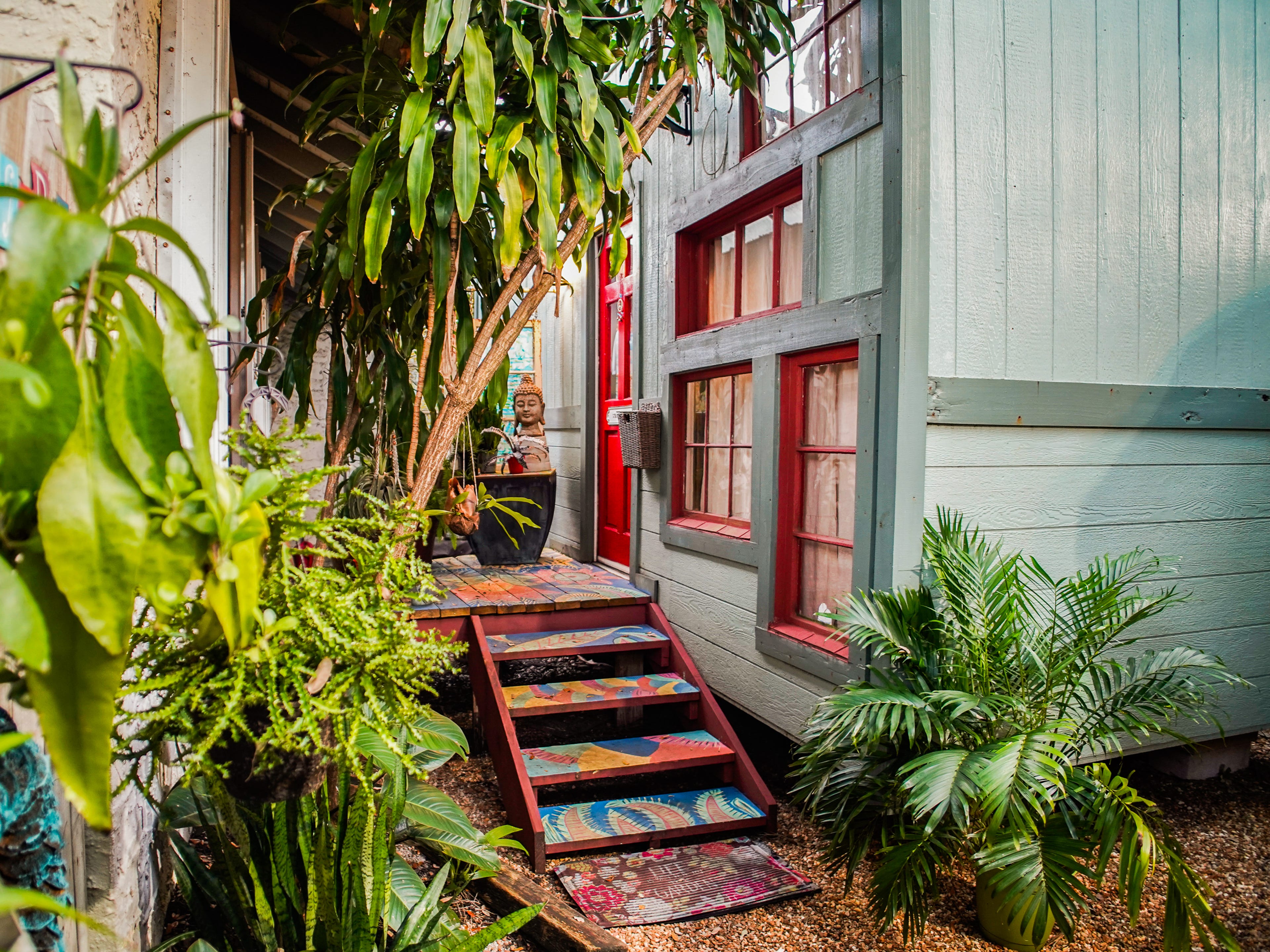 The exterior of a vibrant tiny home with a painted porch and trees on the left