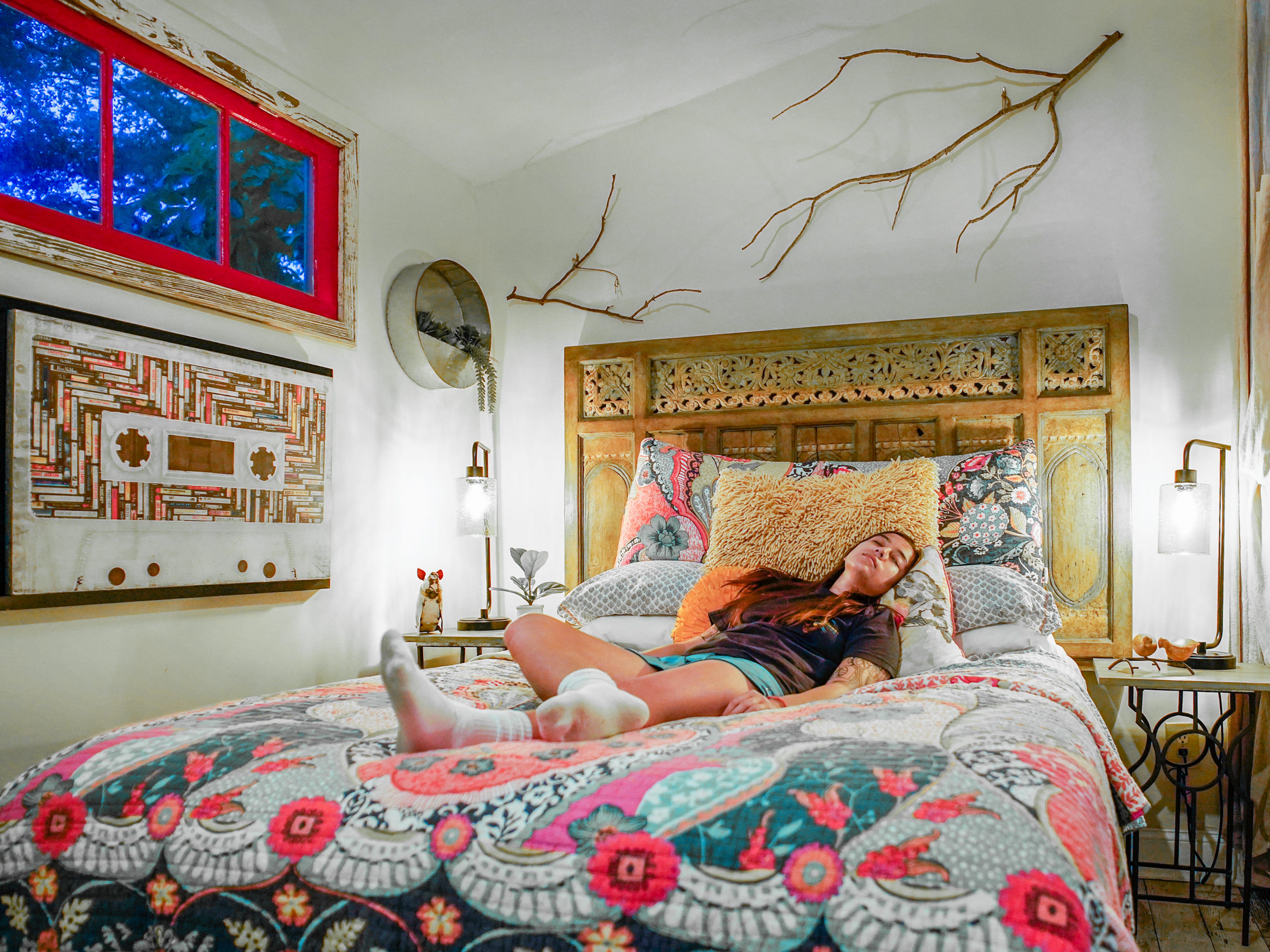 The author rests in a bed with a vibrant quilt and decorated headboard