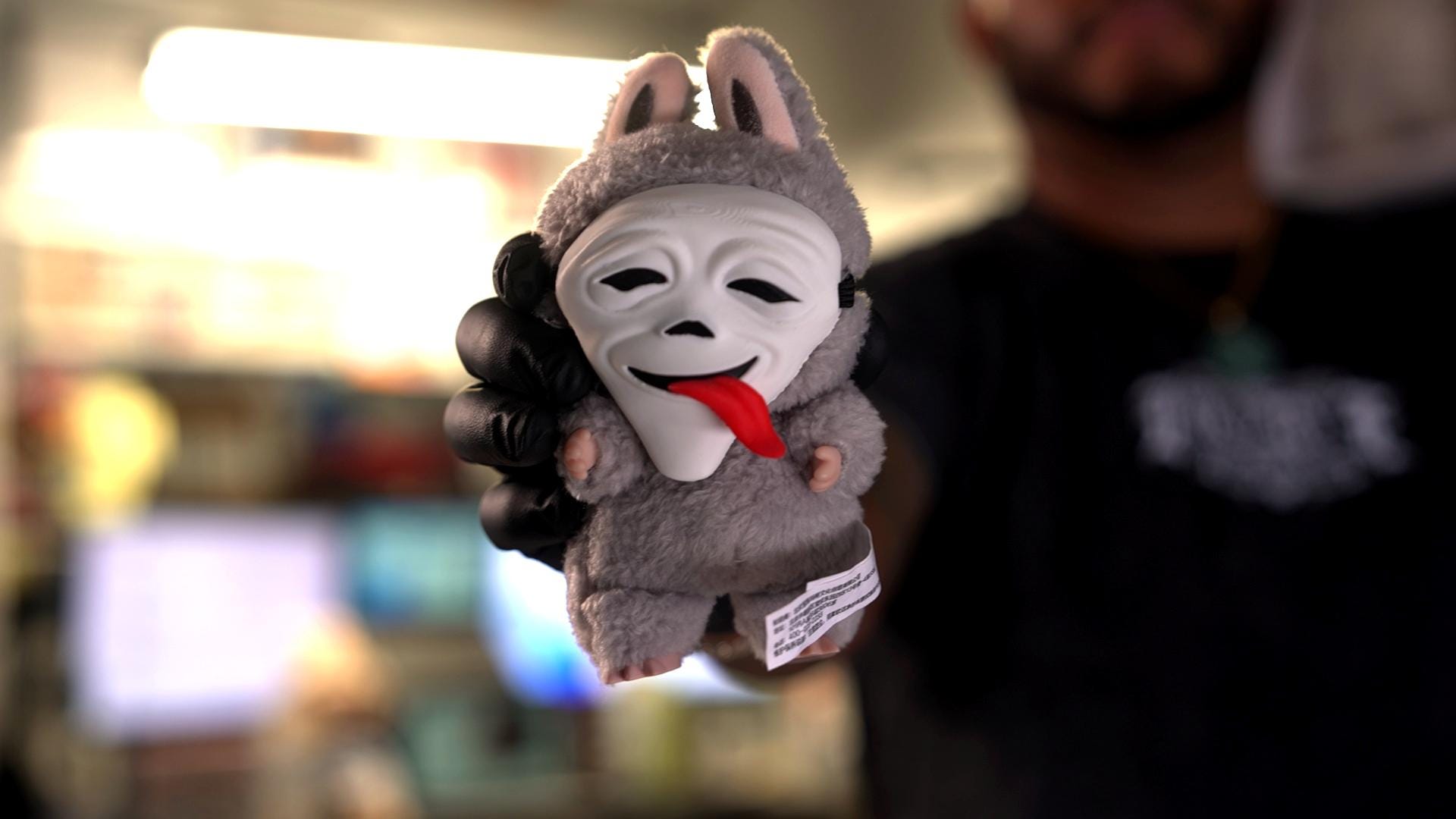 A man holding a gray Labubu with a Scream mask on its face.