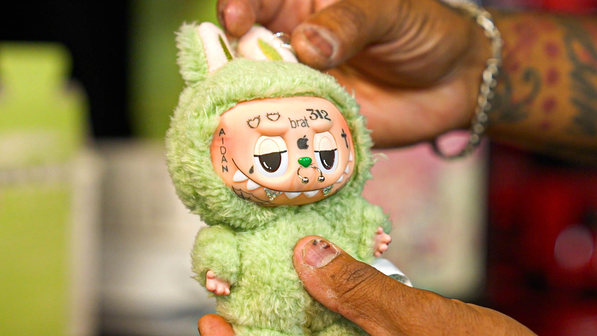 A green Labubu with face tattoos and a nost piercing