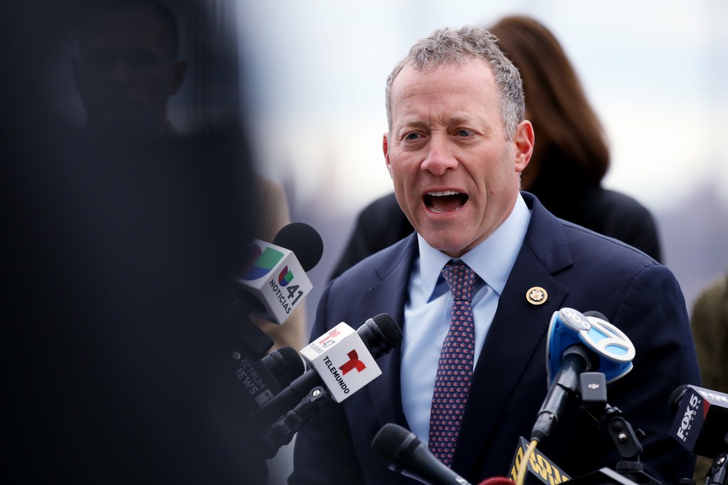 Man in suit speaking into multiple microphones.