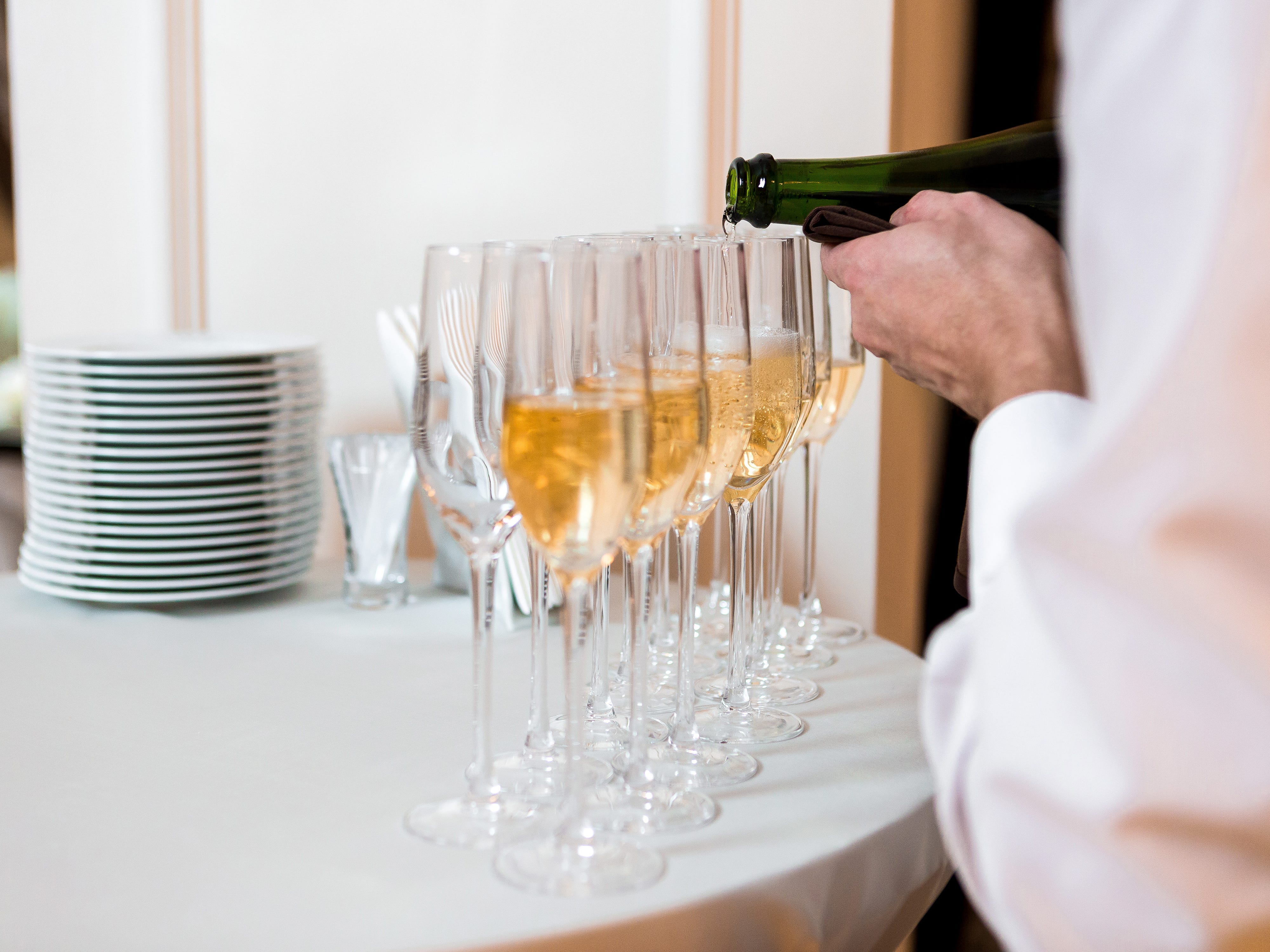 A close-up of a waiter pouring Champagne into glasses.