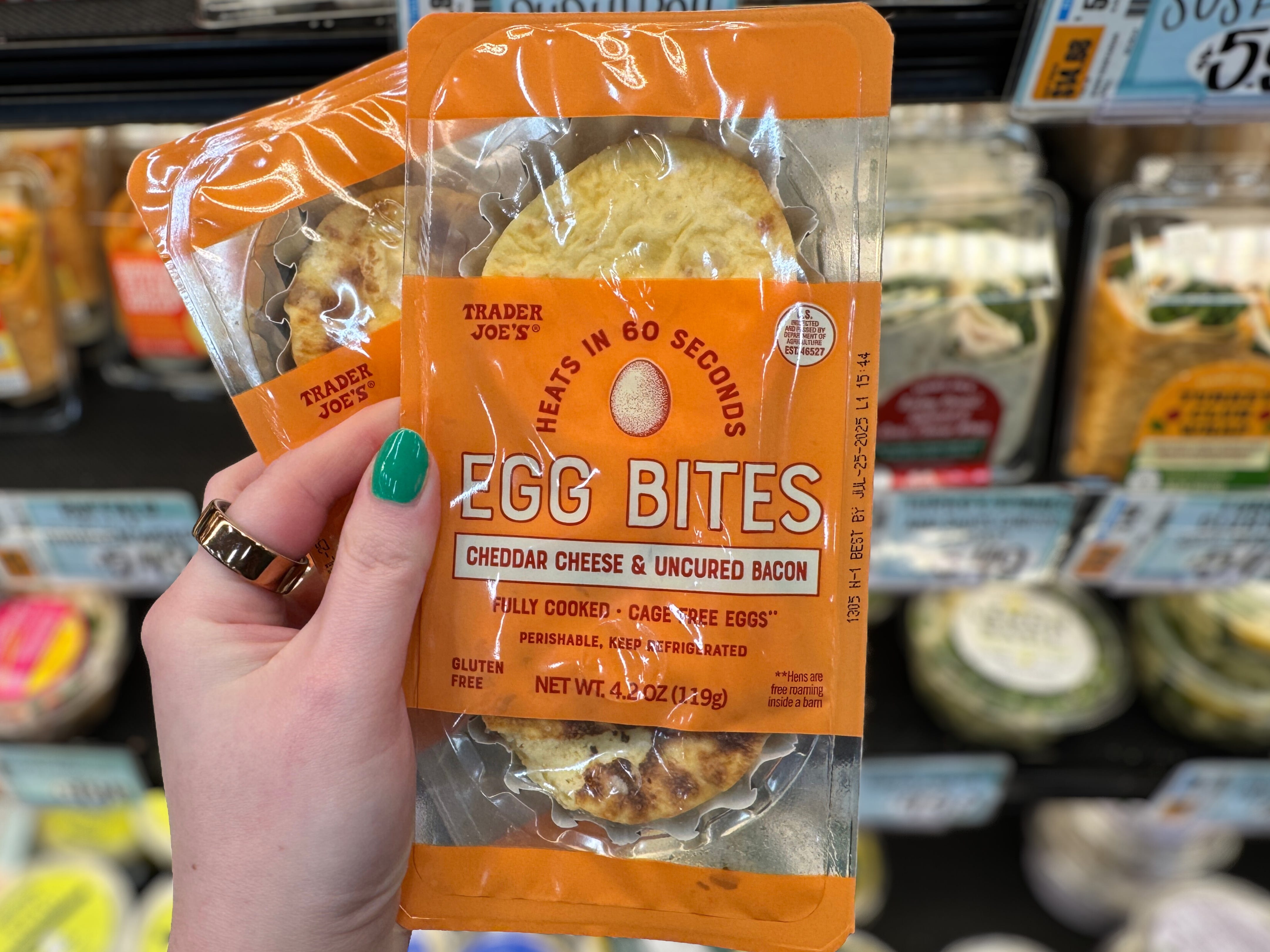 A hand holding packages of Trader Joe's egg bites in the refrigerator section of the store.