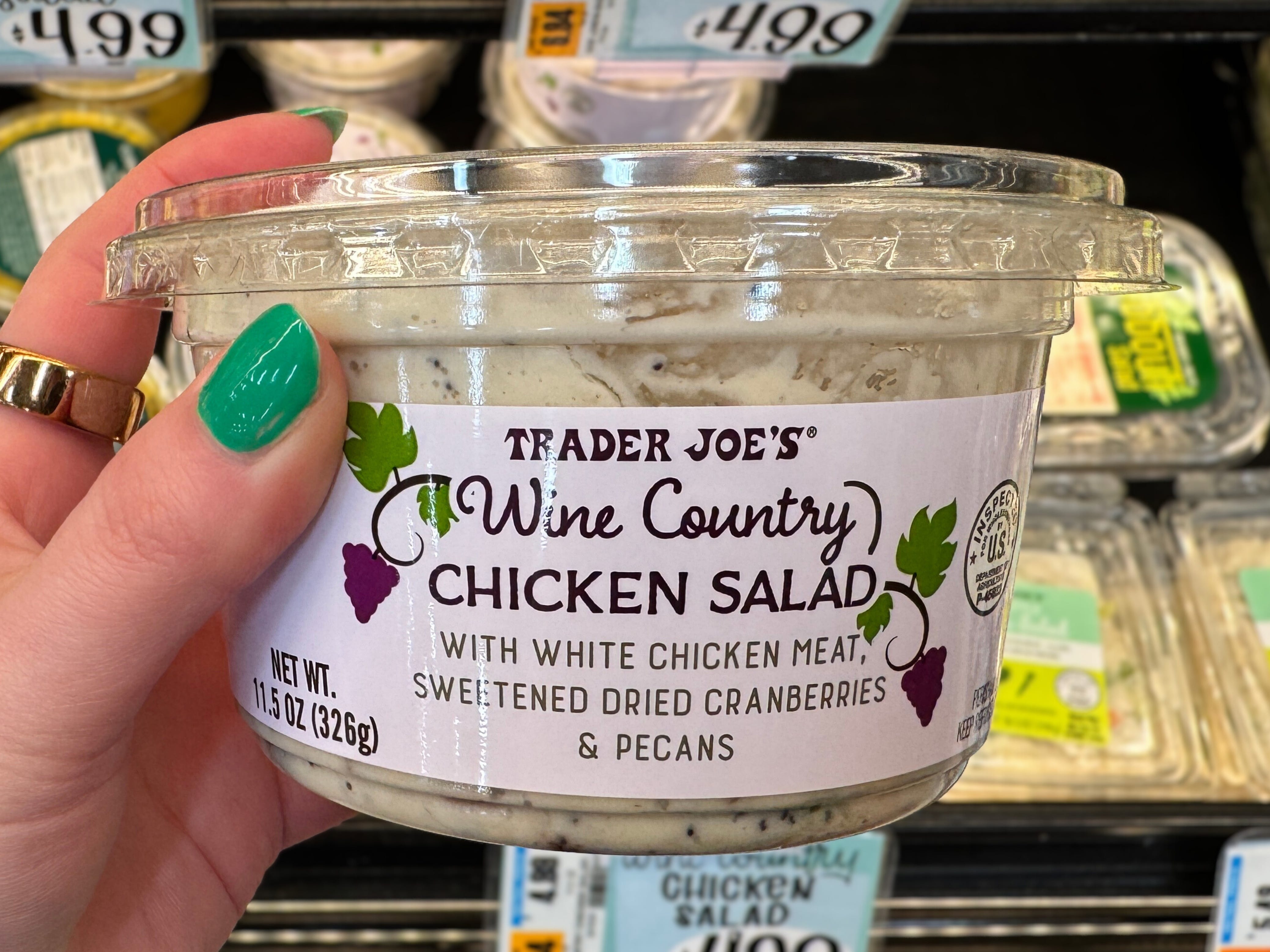 A hand holding a container of Trader Joe's Wine Country chicken salad.