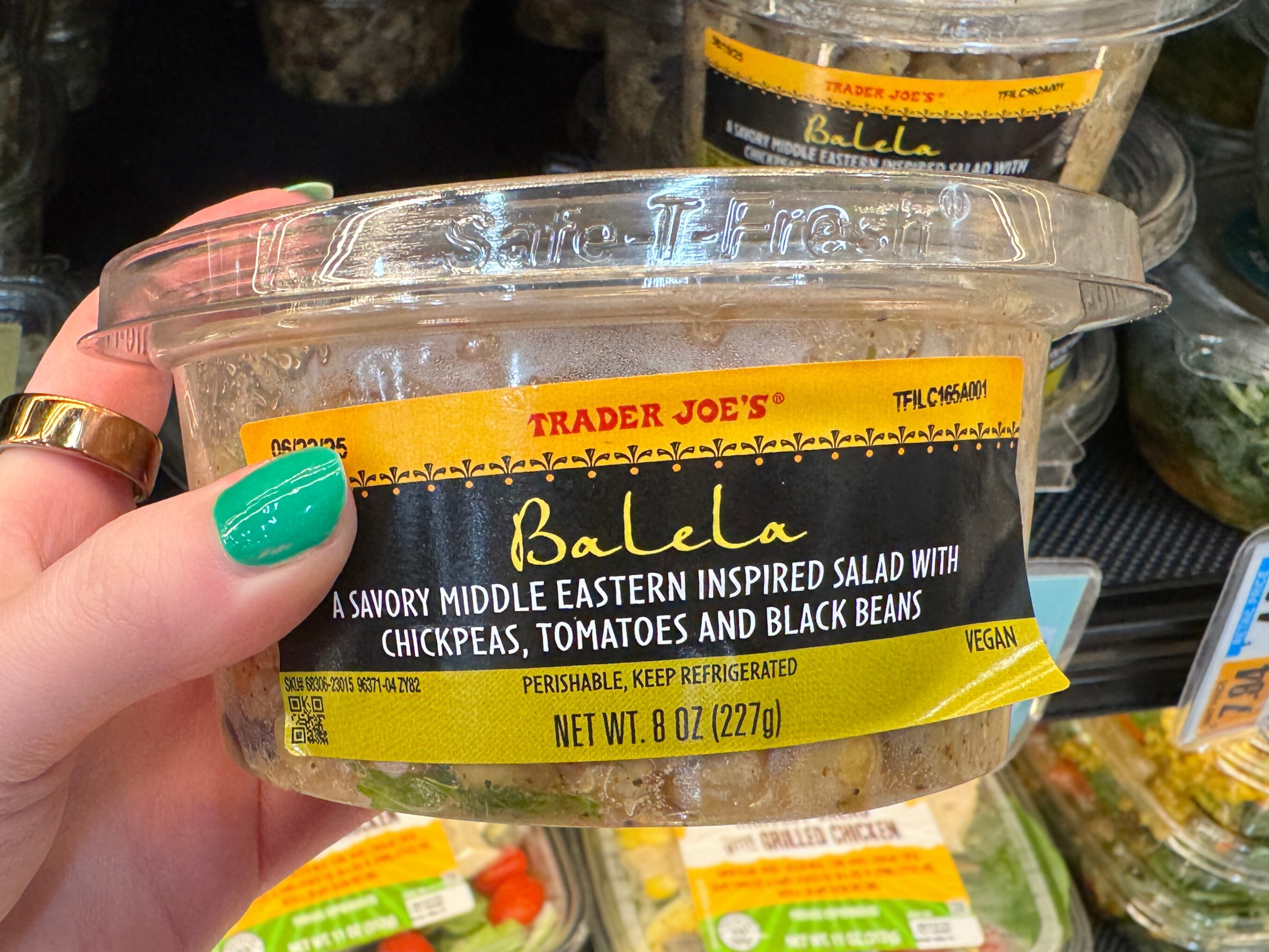 A hand holding a container of Trader Joe's balela salad.