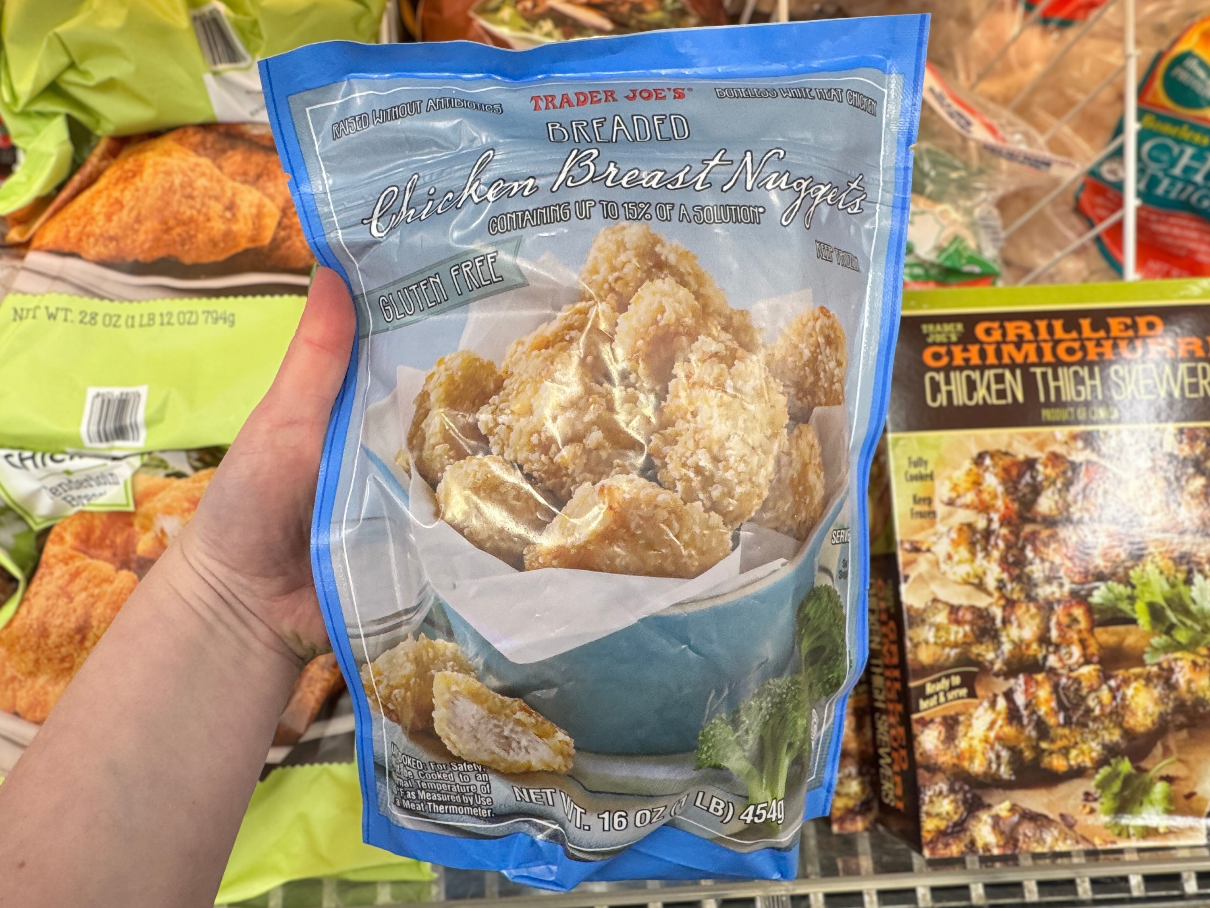 A hand holding a bag of Trader Joe's gluten-free chicken nuggets in the frozen foods section.