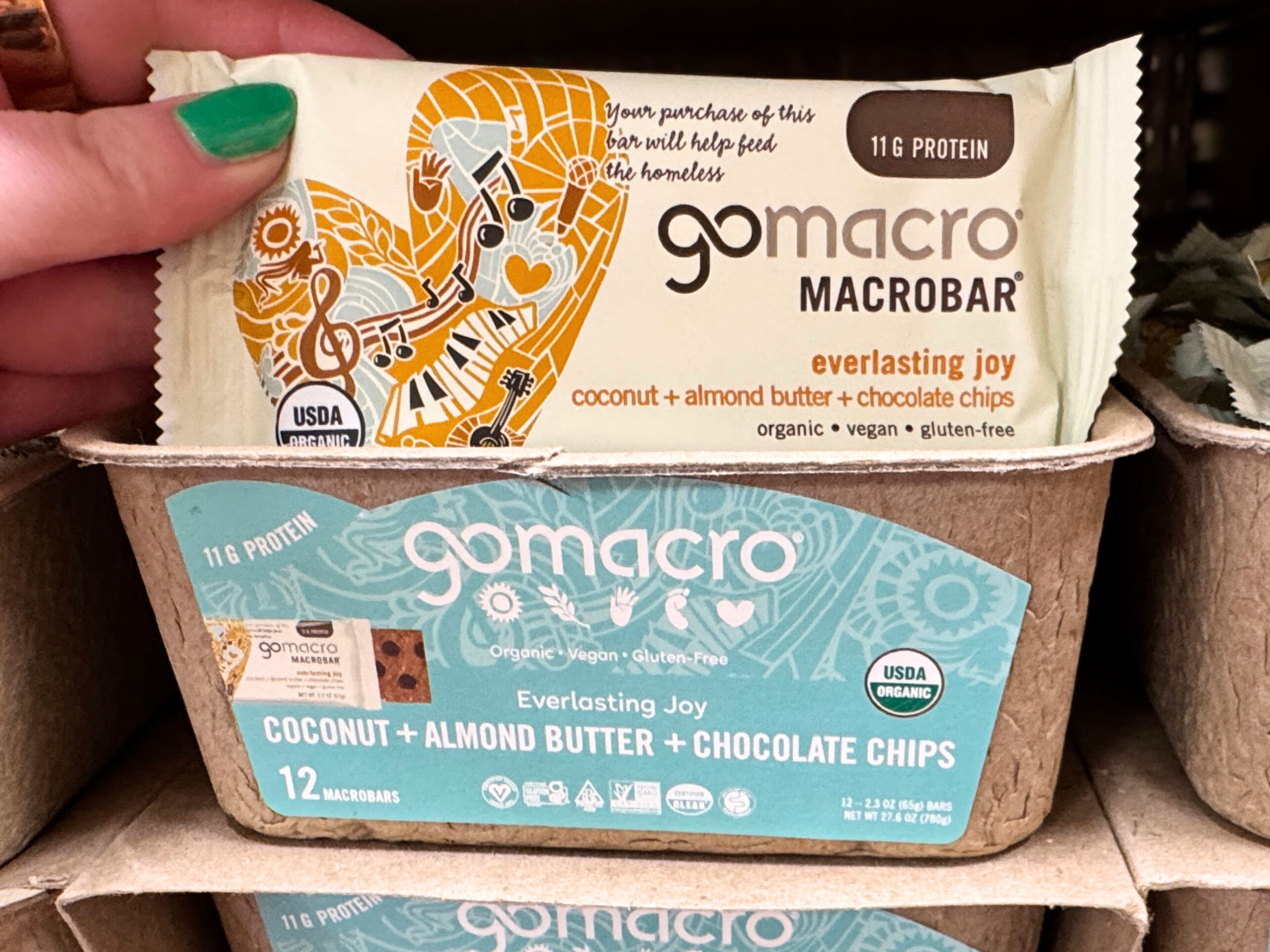 A hand holding a GoMacro bar on display in Trader Joe's.