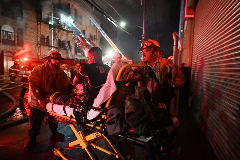FDNY firefighters evacuating a person on a stretcher from a three-alarm fire.