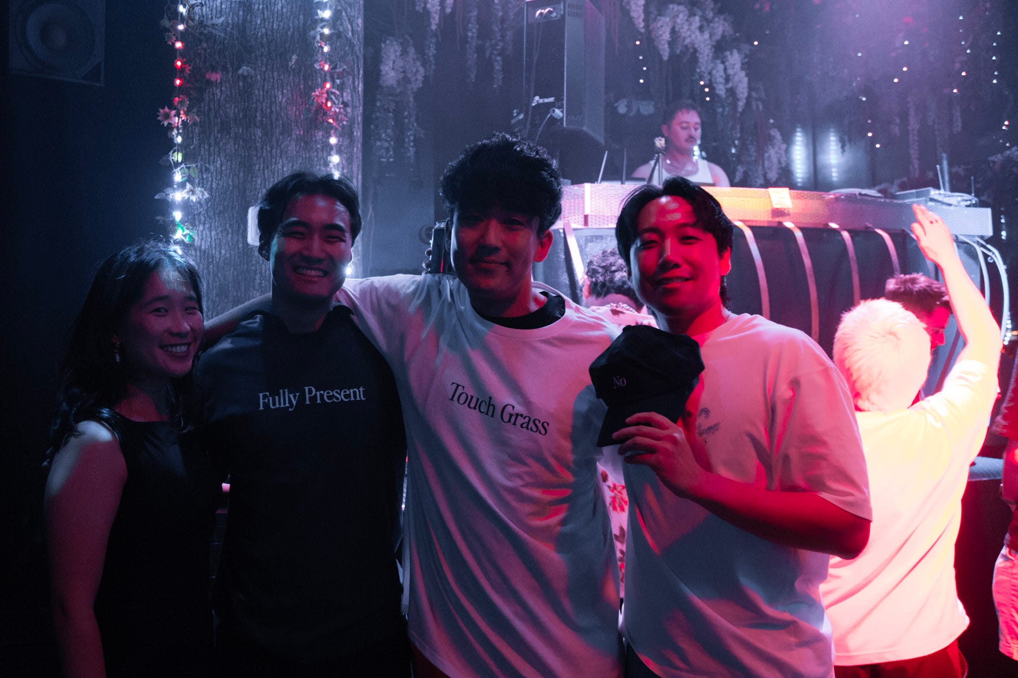 Three men and a woman pose for a photo at a party with arms wrapped around each other's shoulders.