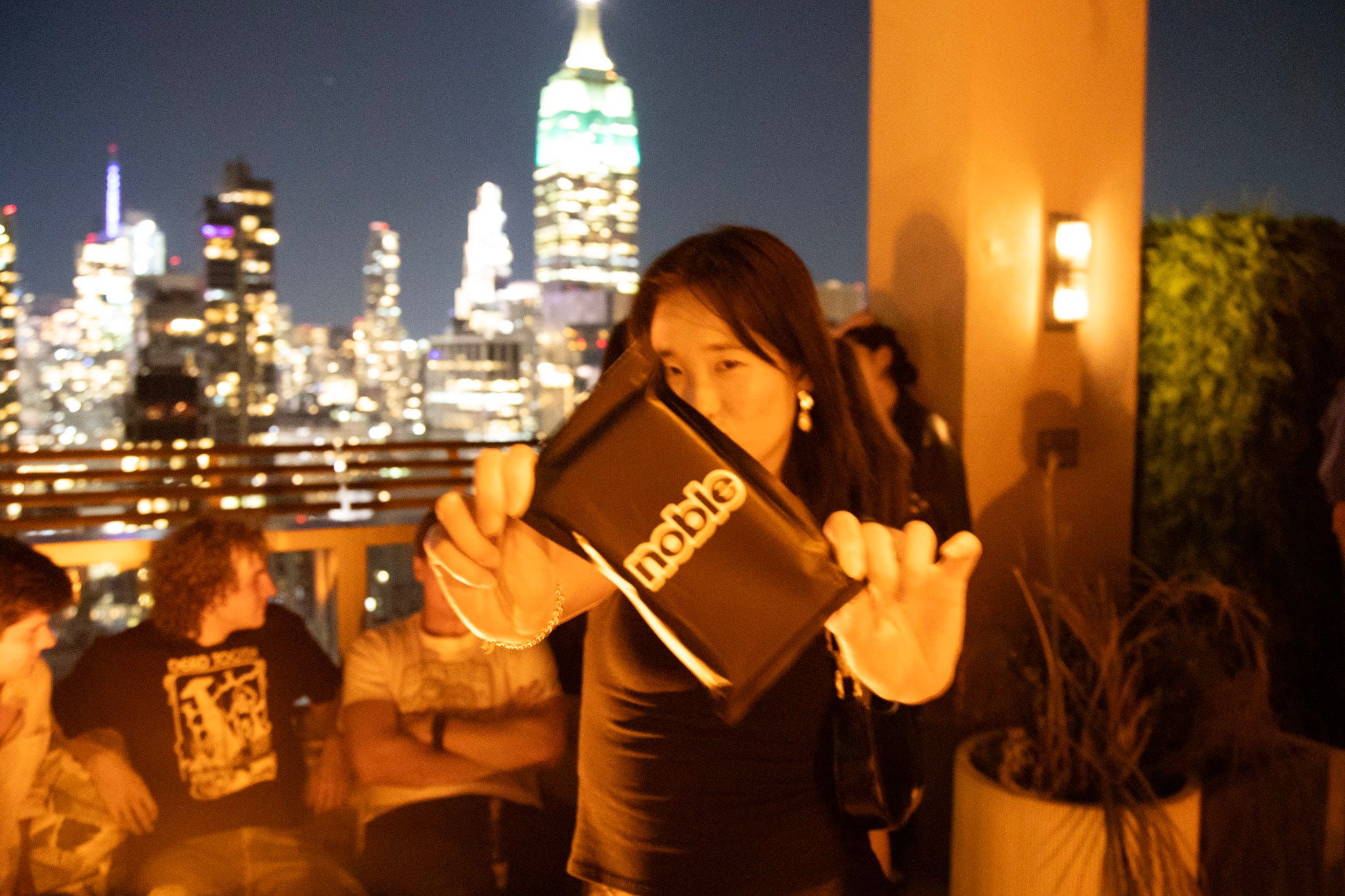 A woman holds up a black phone pouch on a Manhattan rooftop.