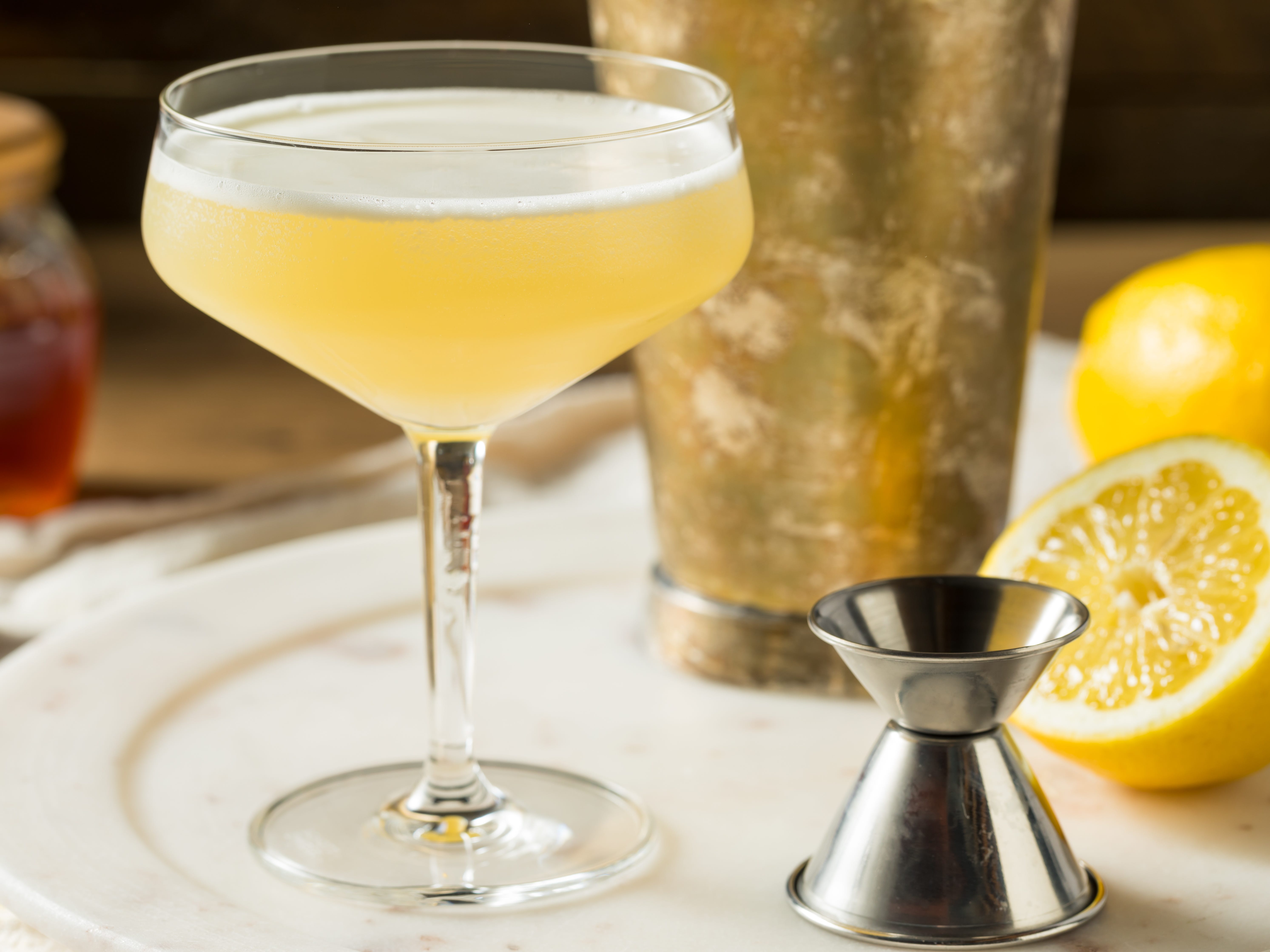 A yellow cocktail on a plate with a jigger.