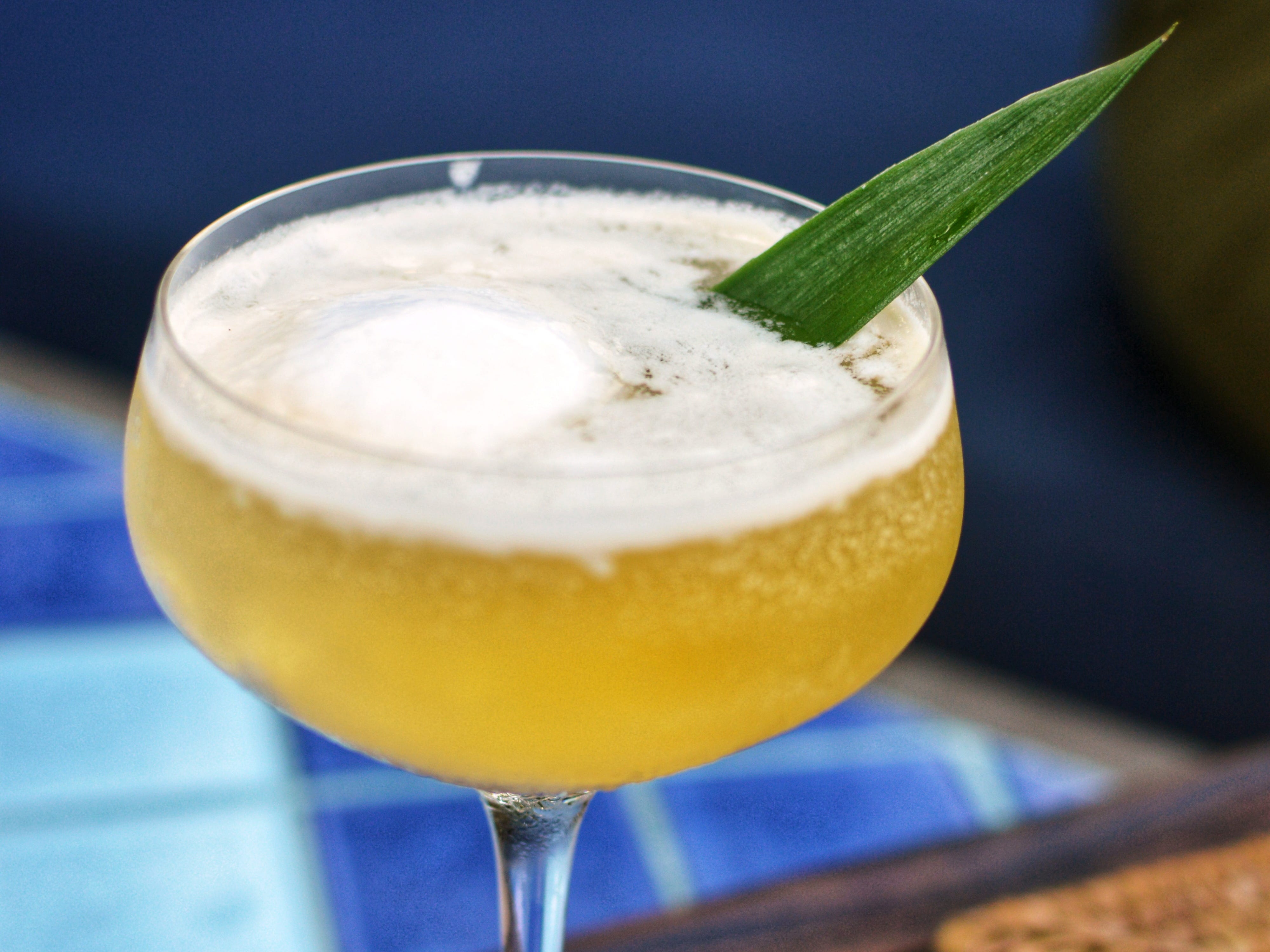 A yellow cocktail with a green leafy garnish.