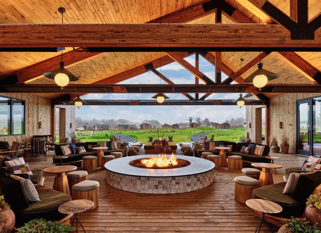 Outdoor lounge area with a large fire pit and comfortable seating, overlooking a field.