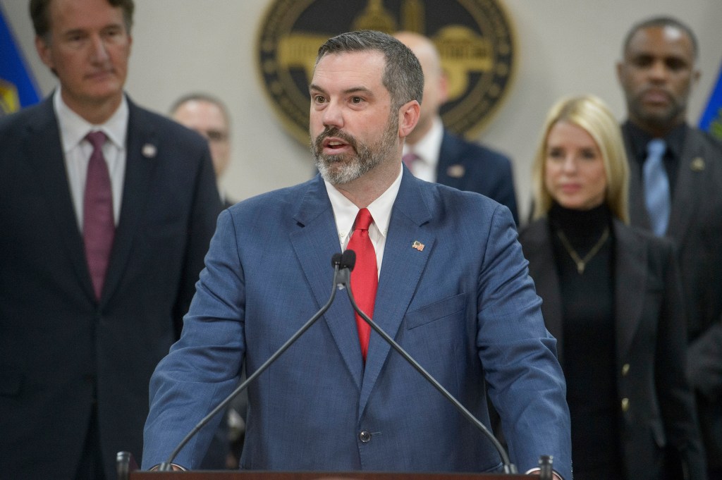 Erik Siebert speaking at a news conference with Glenn Youngkin and Pam Bondi listening.